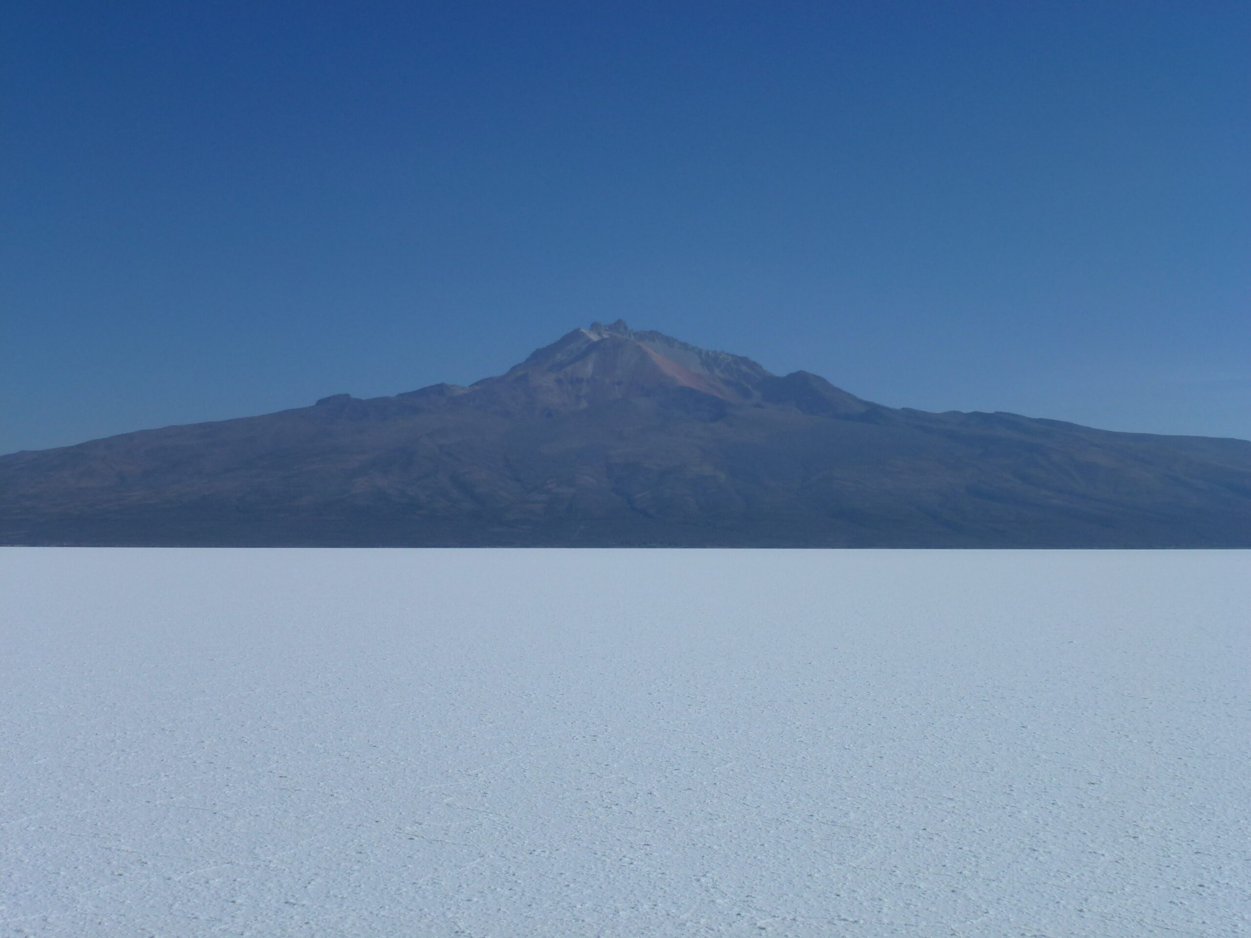 白いウユニ塩湖の向こうにそびえるトゥヌパ山