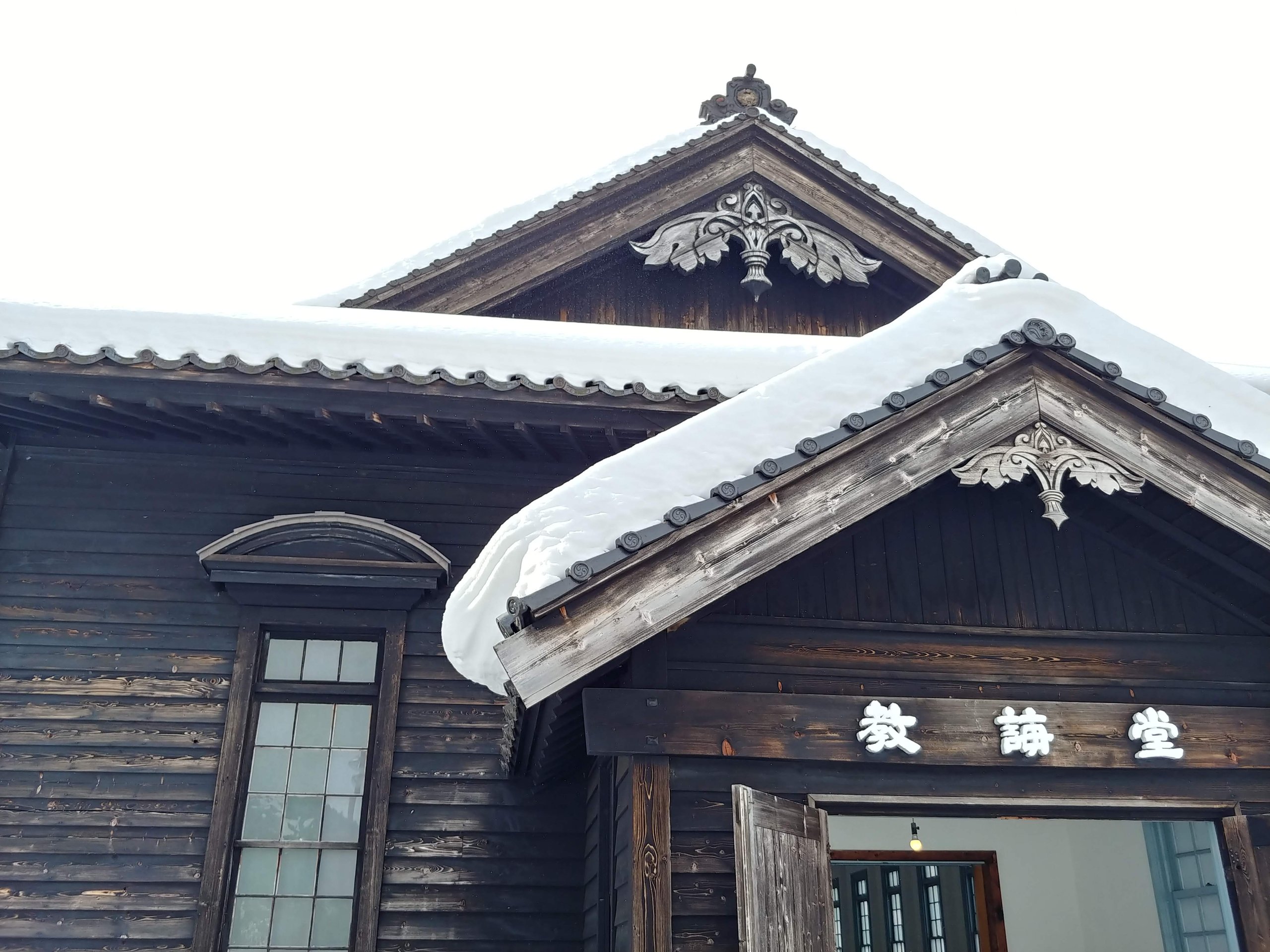 雪をかぶった木造の教誨堂の屋根と飾り