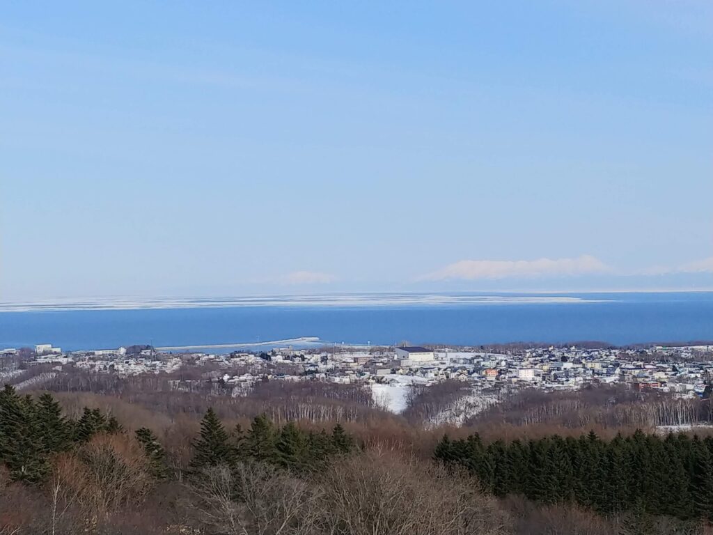 天都山から見た網走の街と、沖に白く続く流氷の帯