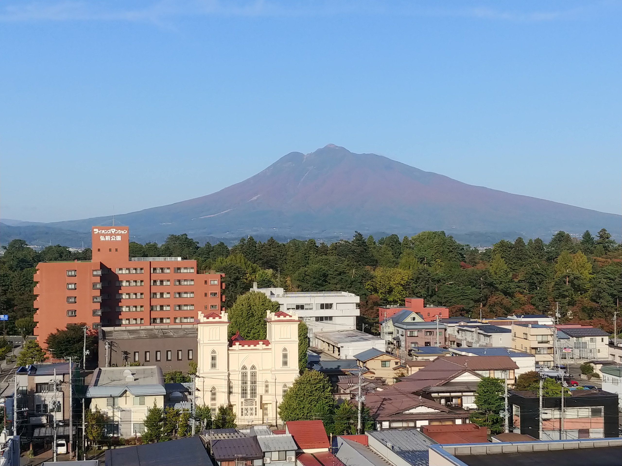 弘前の街並みの向こうにそびえる、中腹が紅葉した岩木山