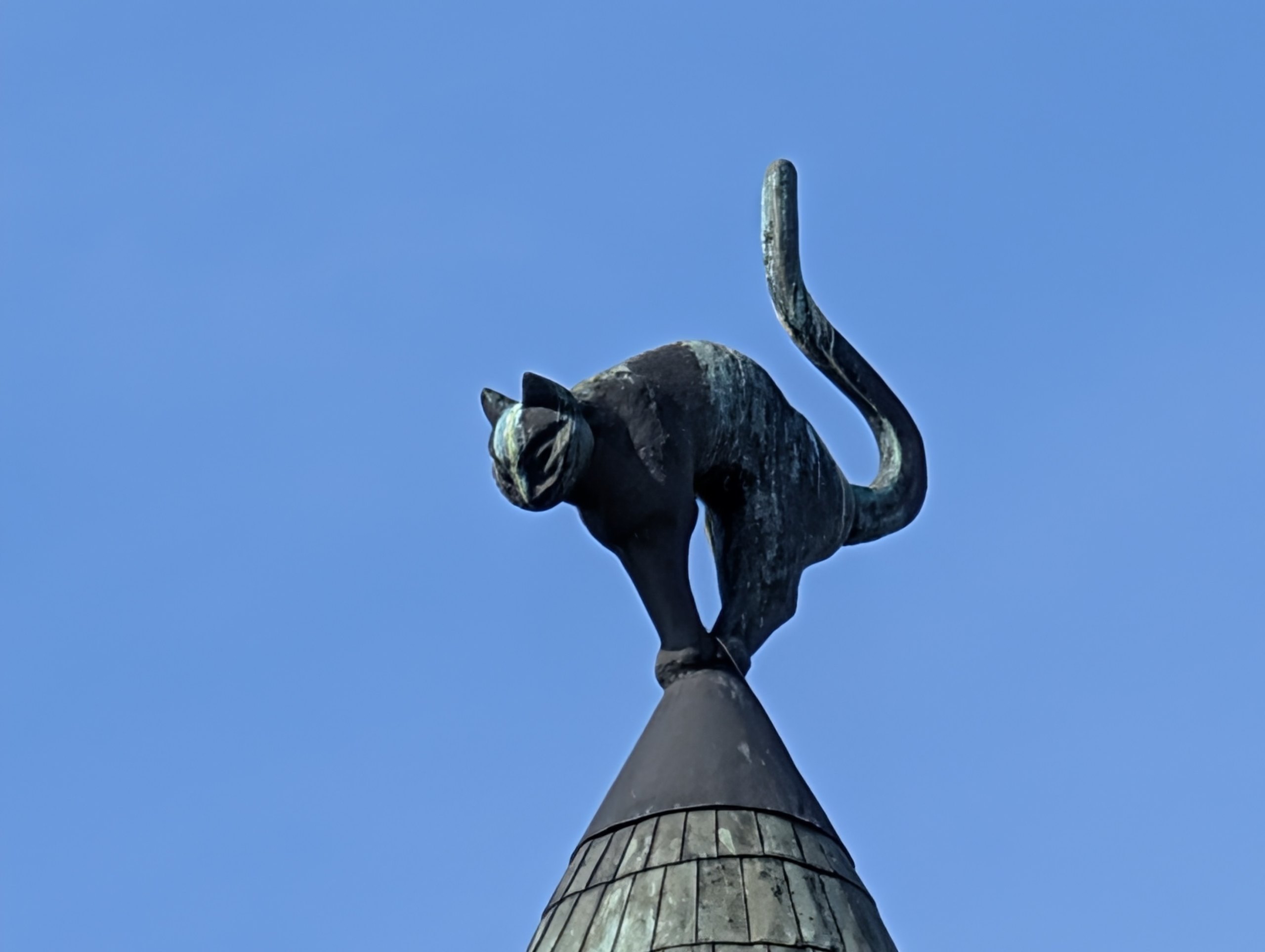 とんがり屋根の上で、背中を丸めた猫の像