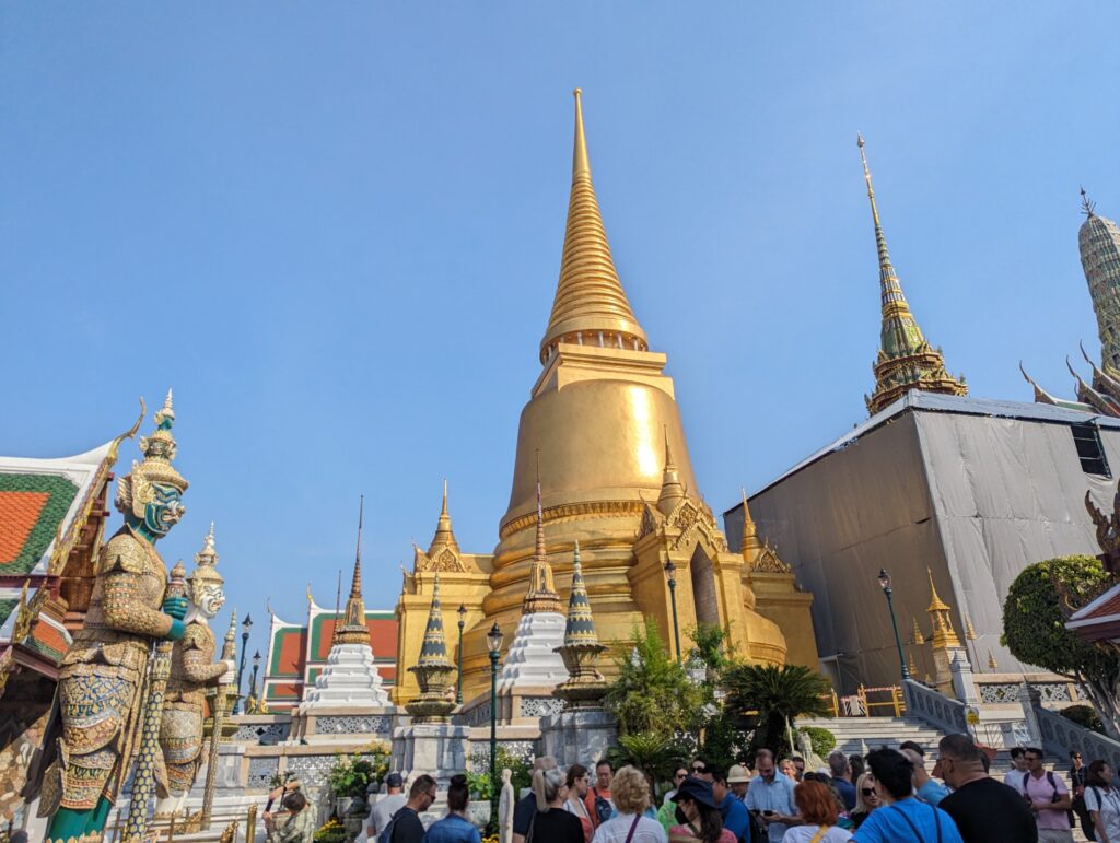 青空にそびえる金色の仏塔と、門を守る鬼の像