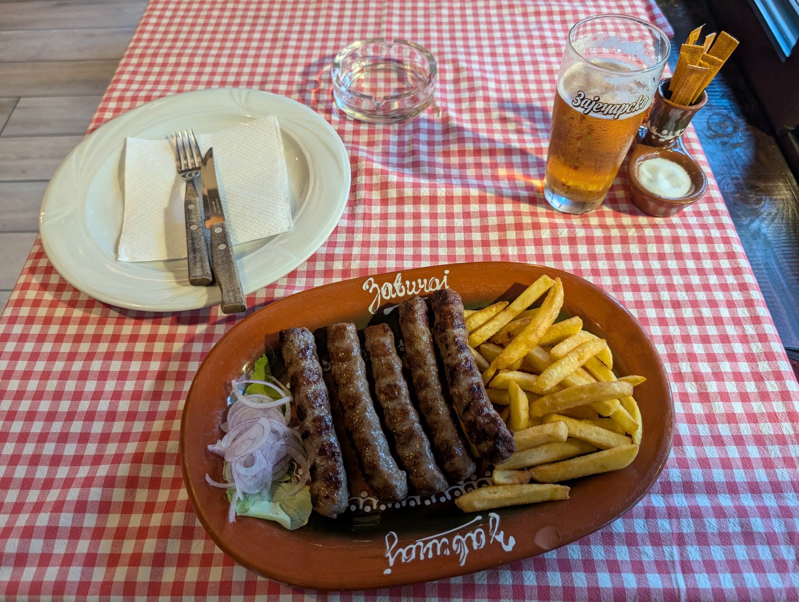 赤いチェックのテーブルクロスの上の、チェバピとフライドポテトとビール