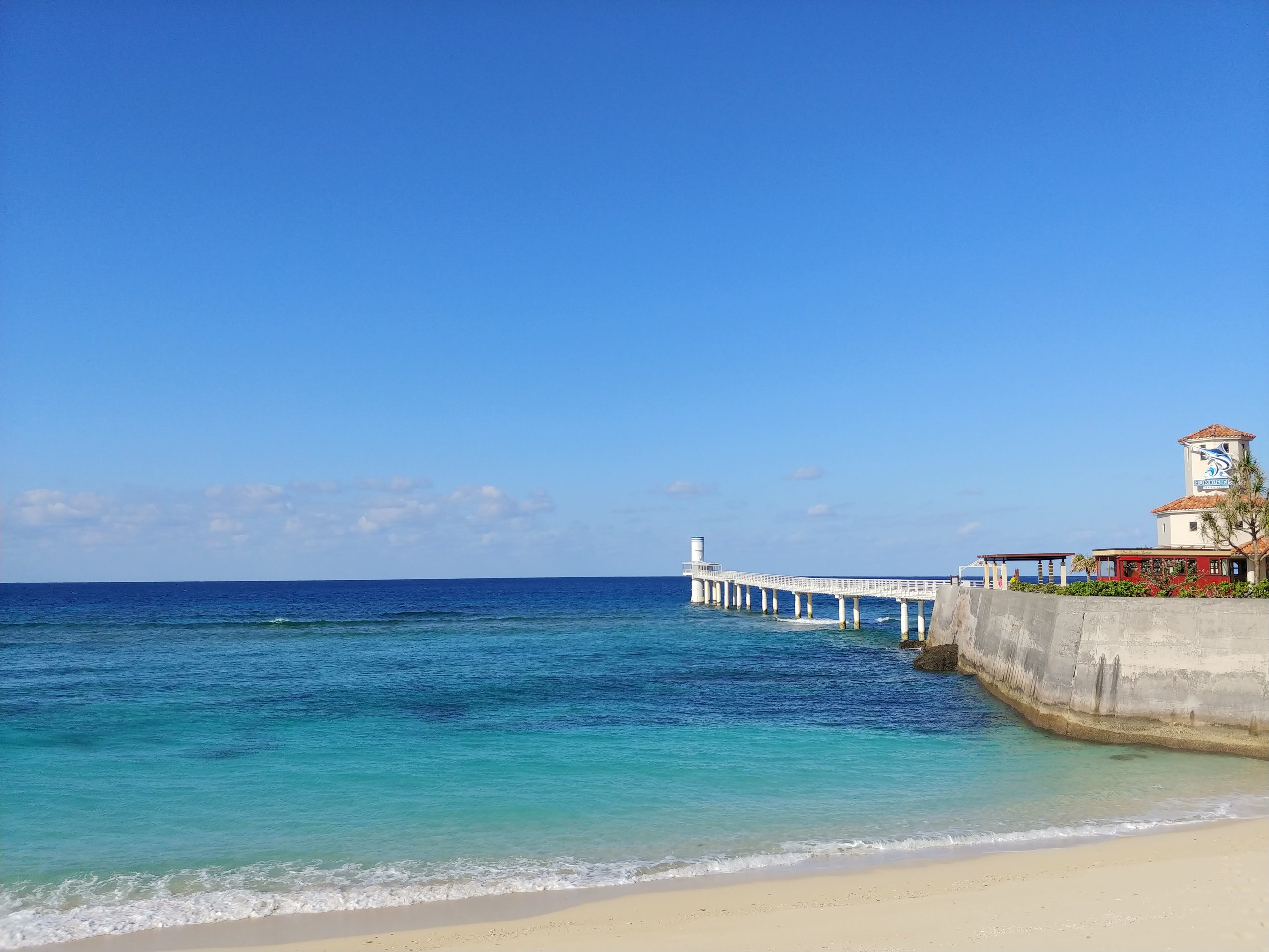 青い海に延びる白い桟橋と、その先の海中展望塔