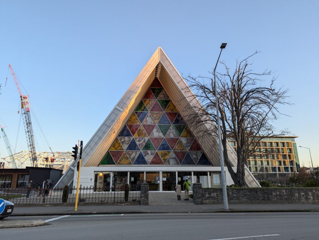 夕方の空の下に建つ、三角屋根と色とりどりのステンドグラスのカードボード大聖堂