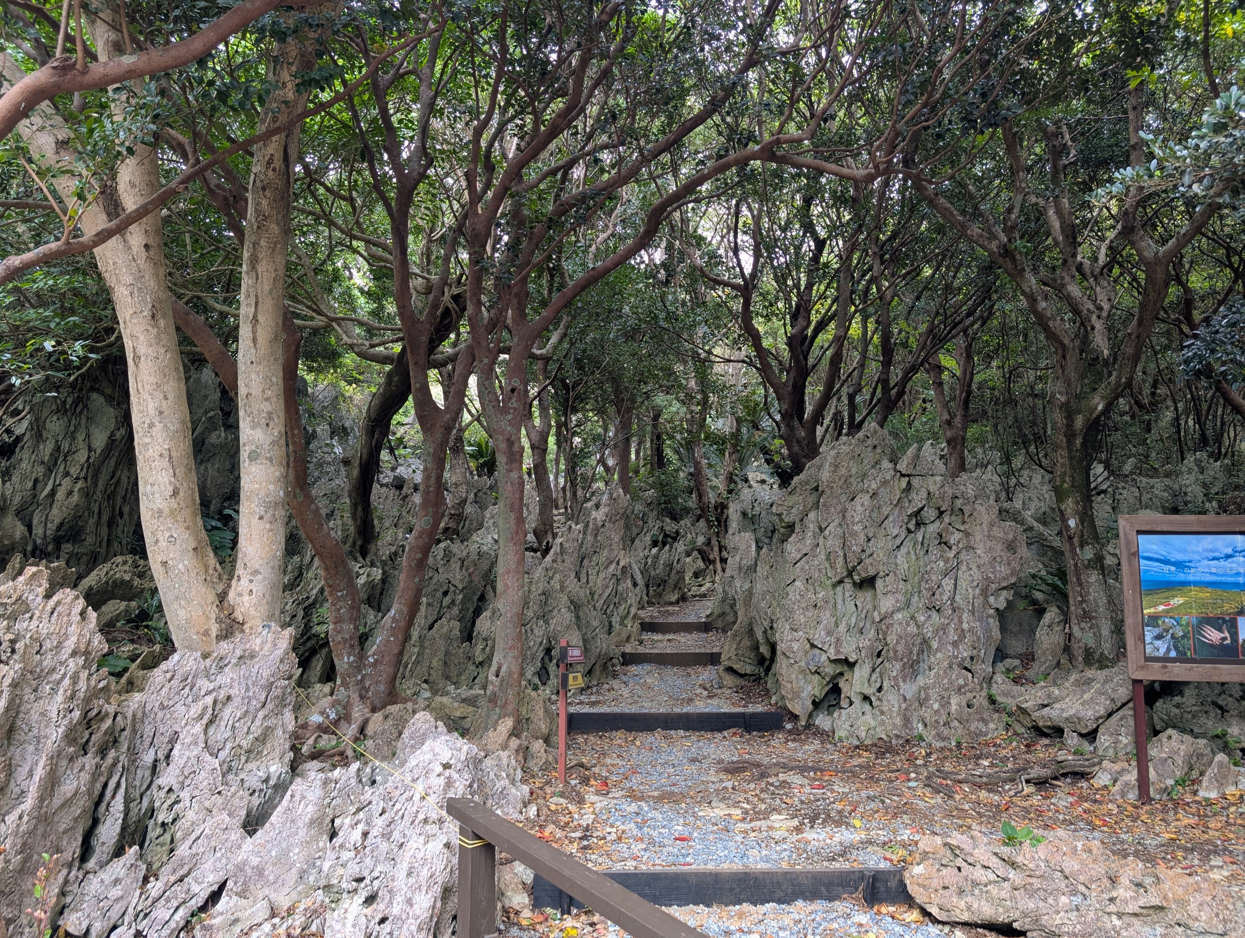 岩の間を抜ける砂利と階段の小道。右手に案内板