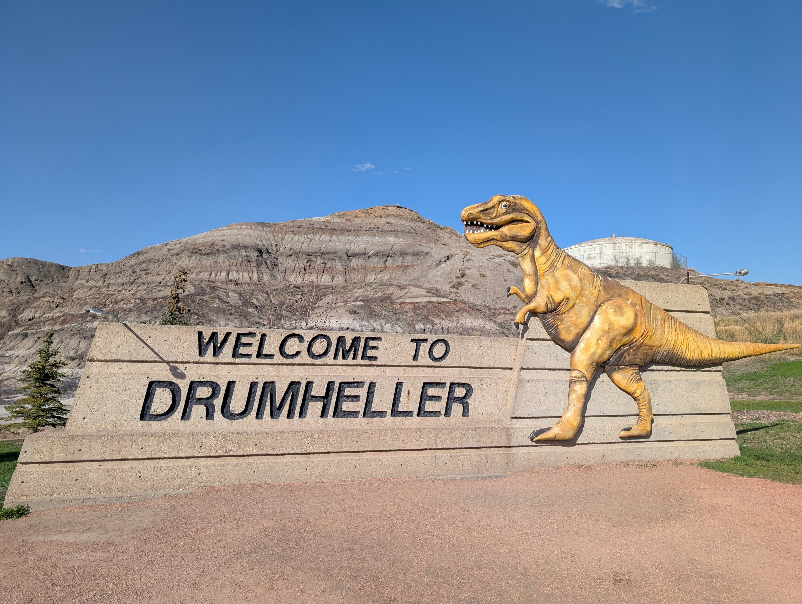 「WELCOME TO DRUMHELLER」の文字と、金色のティラノサウルスの像