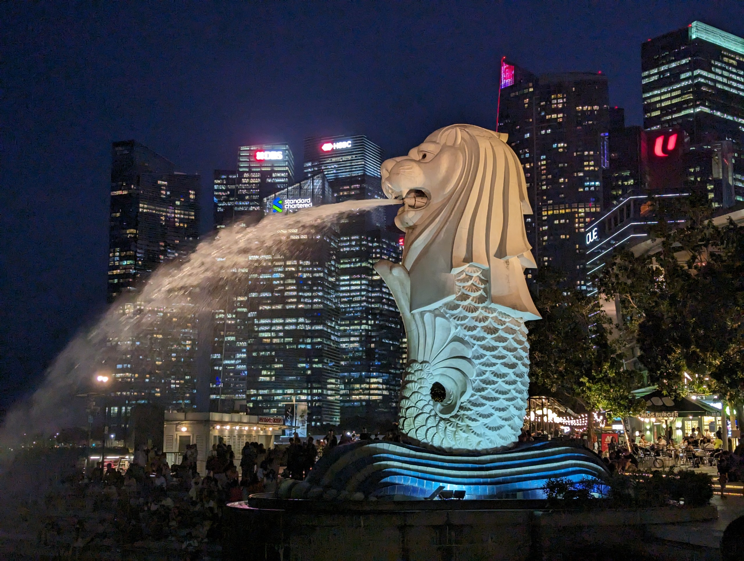 夜の高層ビルを背に、口から水を吐くマーライオン