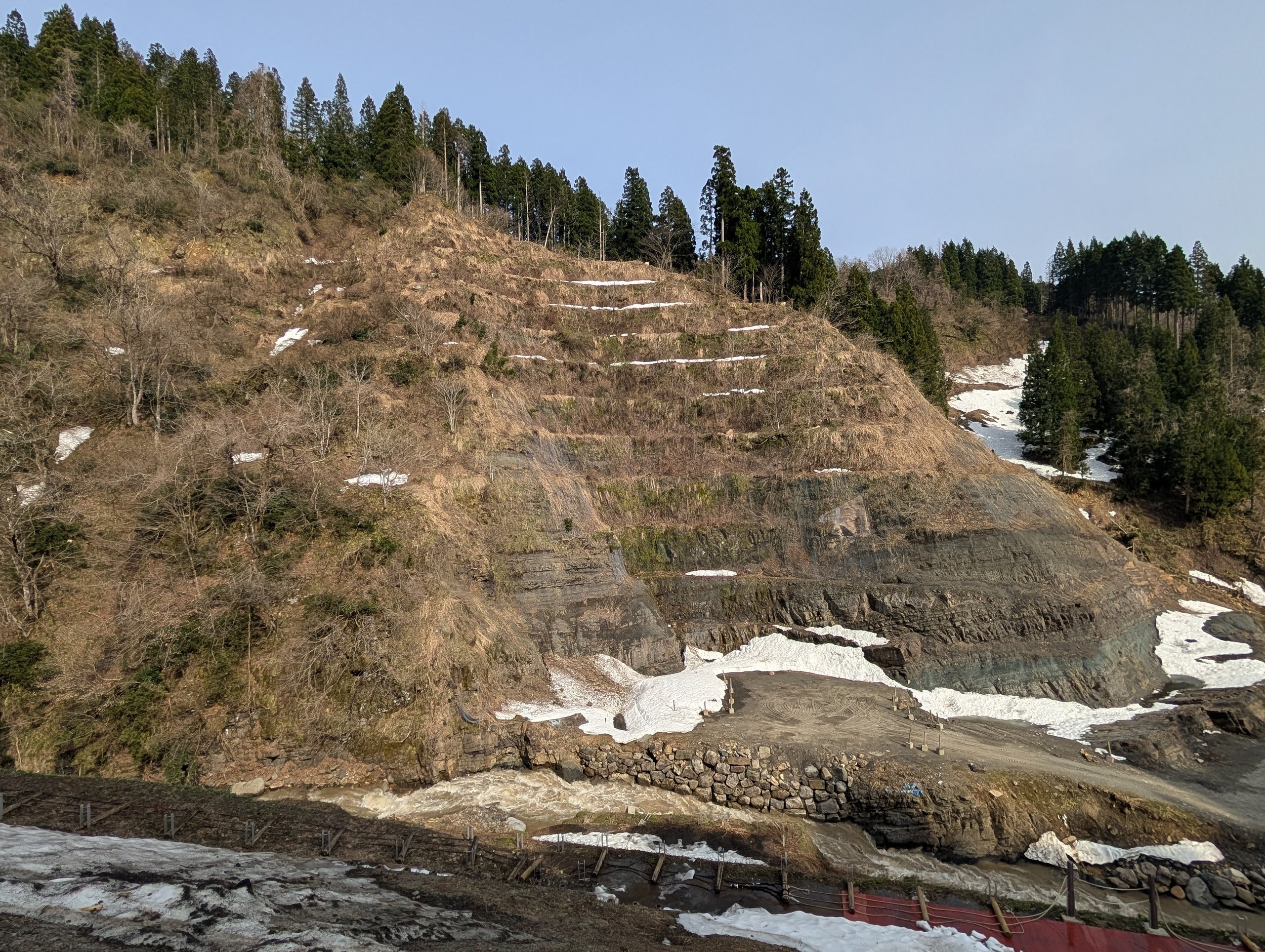 雪が少し残る、しま模様の地層の崖