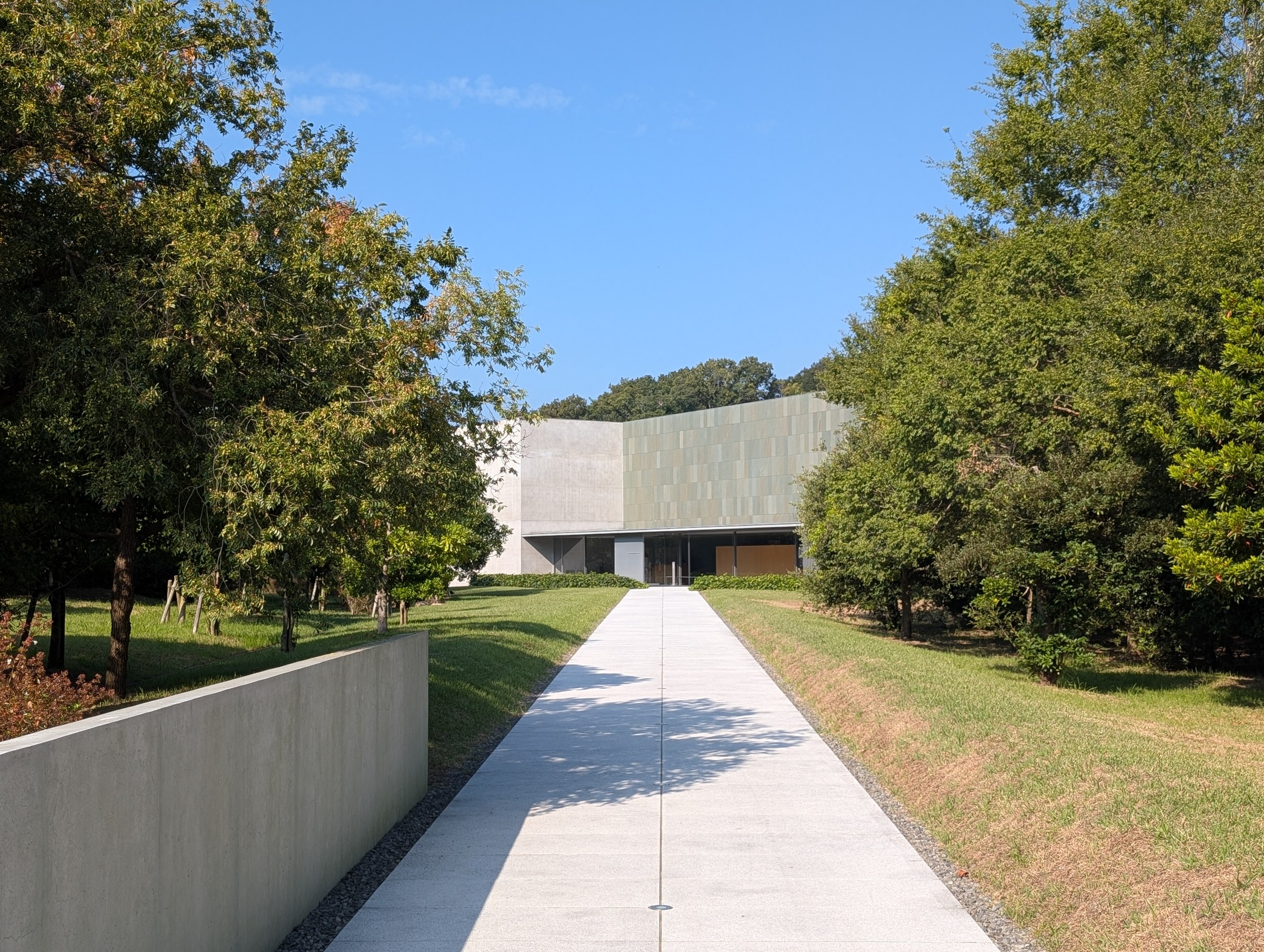 木々の間をまっすぐ伸びる道と、美術館の建物