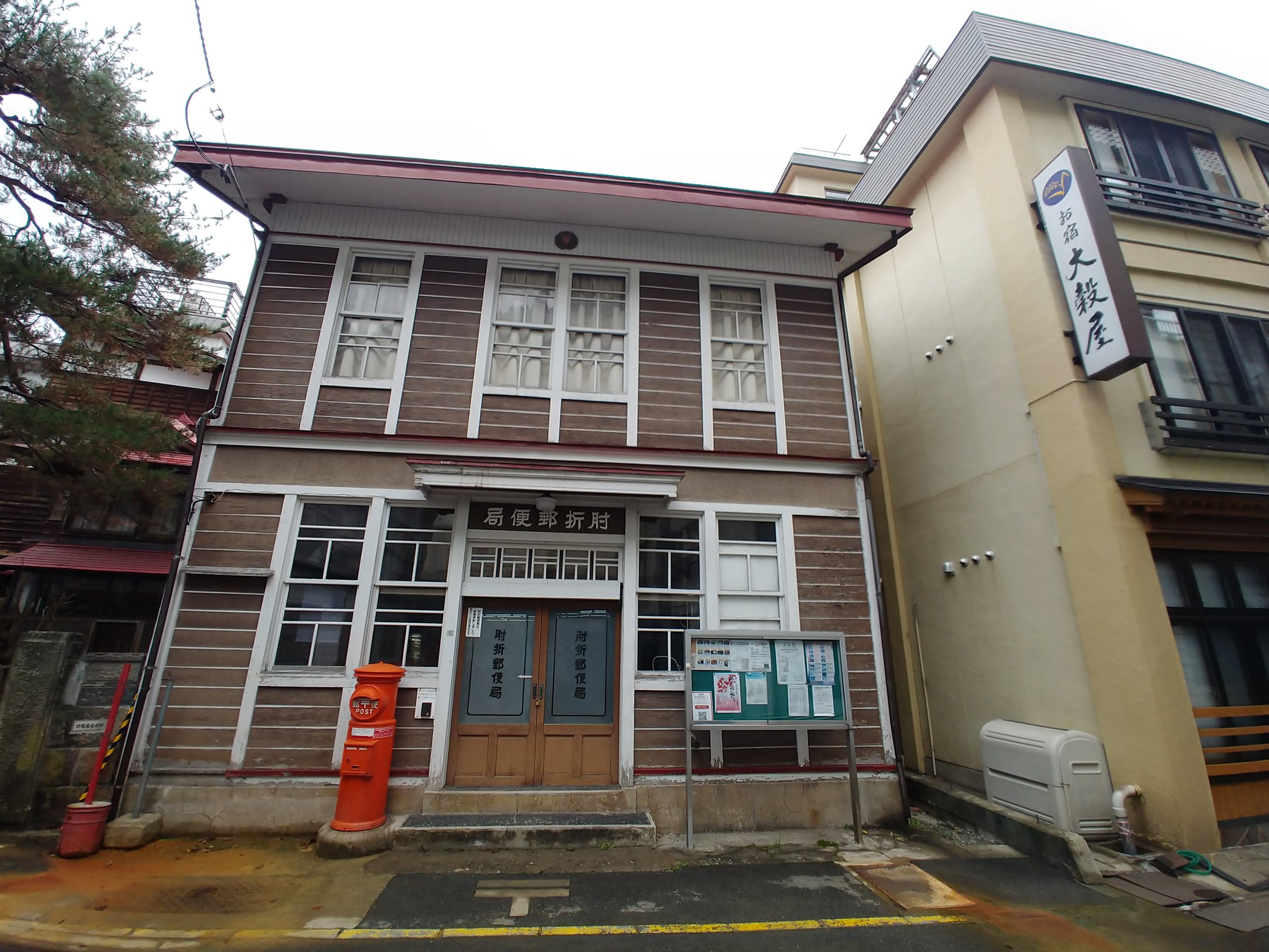 赤い丸ポストが立つ、古い木造の肘折郵便局