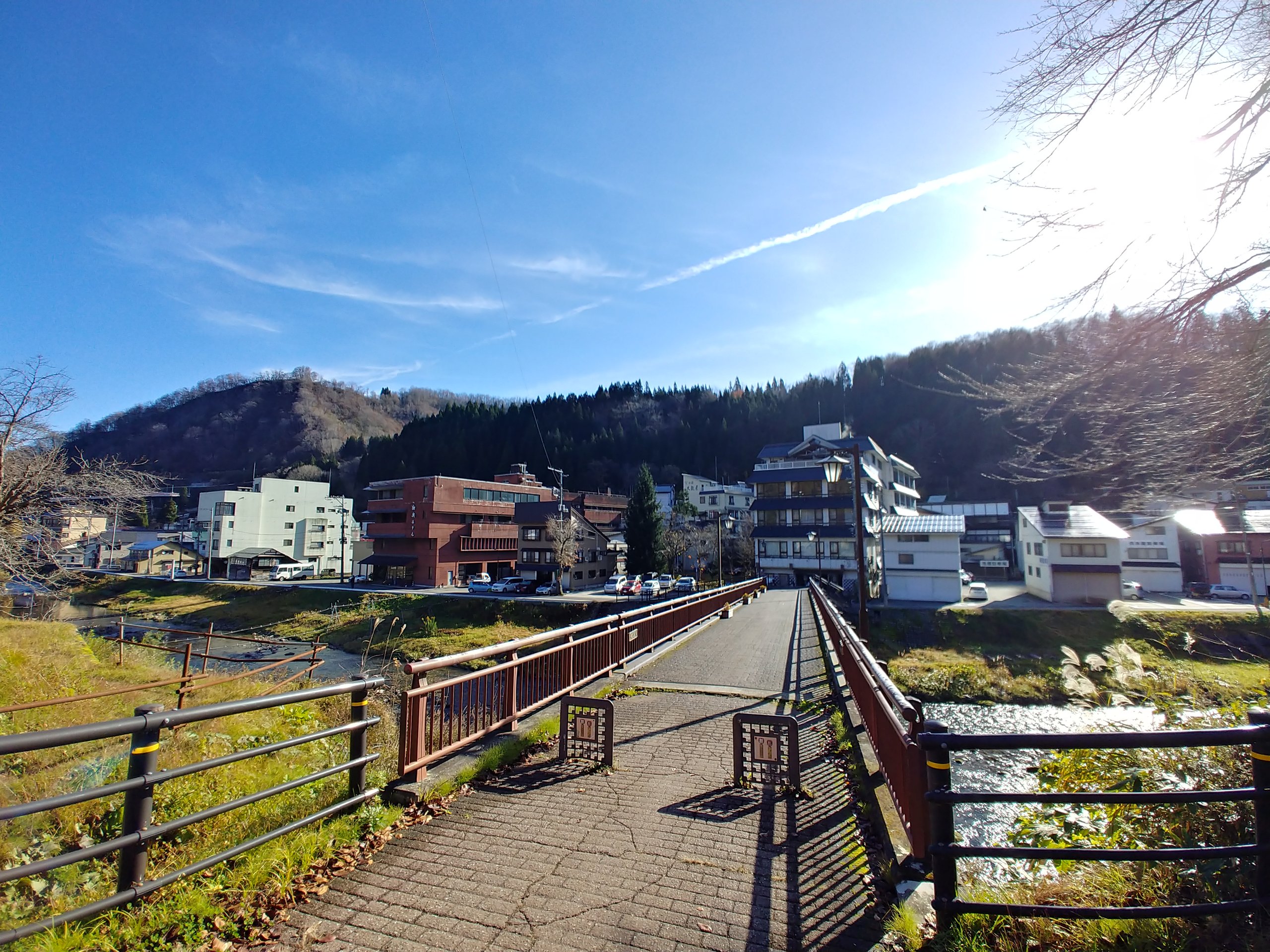 青空の下、川に架かる橋と山あいの建物