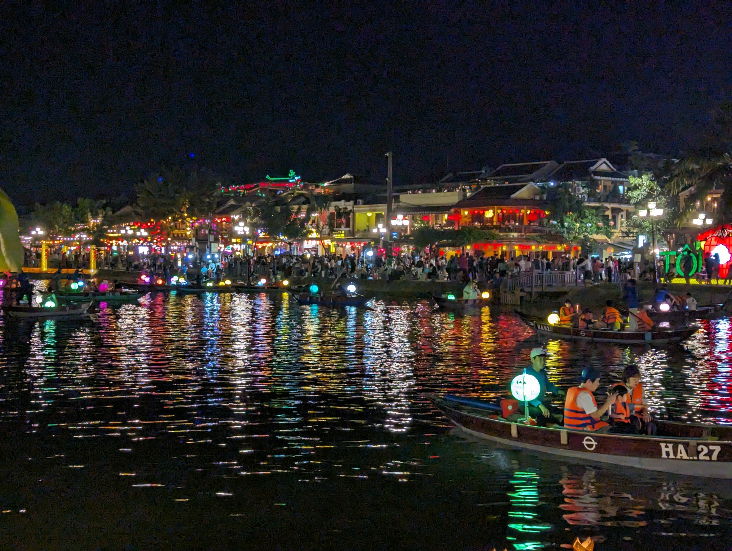 色とりどりの灯りが映る夜の川と、灯籠を浮かべる舟