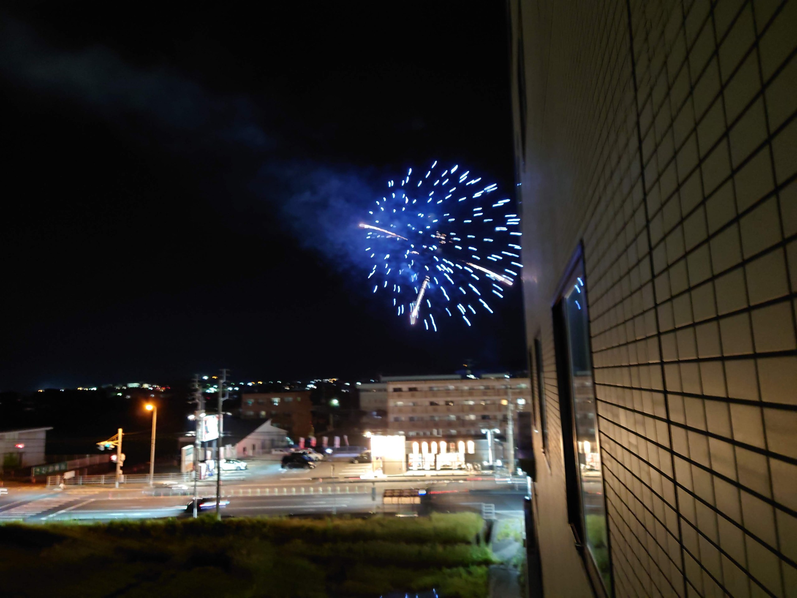 夜空に開く青い花火と、ホテルの外の街明かり