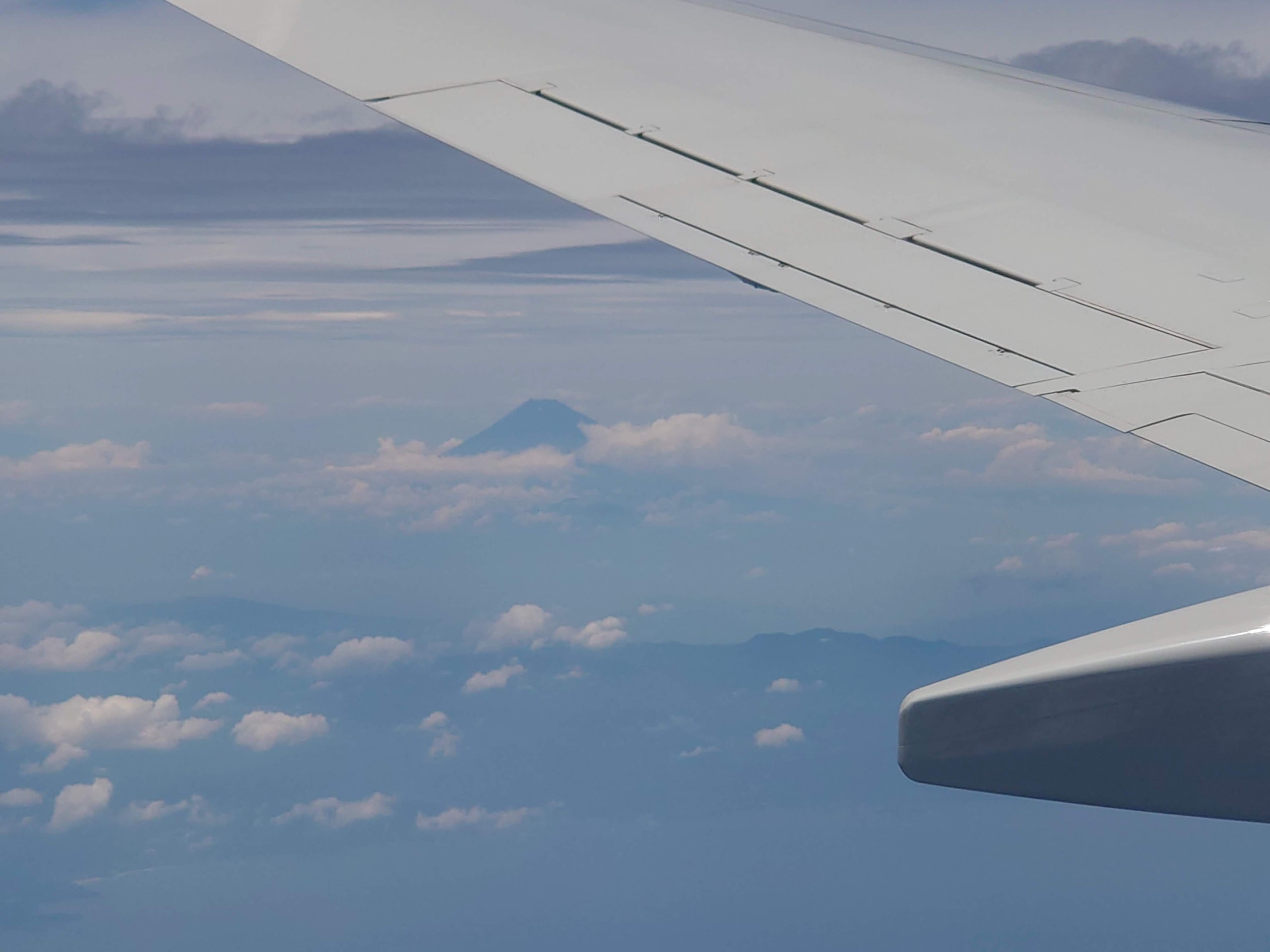 飛行機の翼の向こうの雲の上に見える富士山