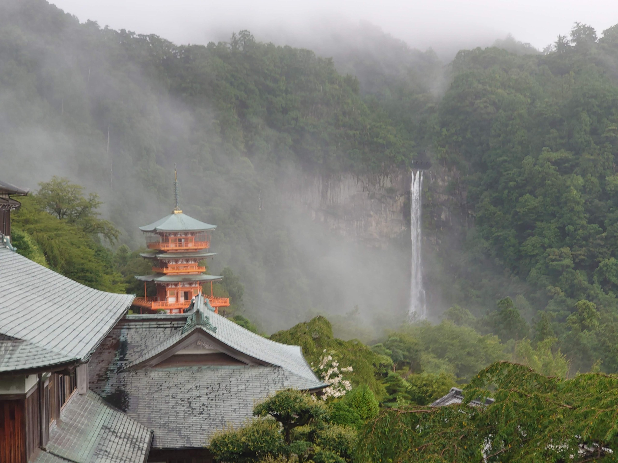 朱色の三重塔の向こうに、雲の中から落ちる那智の滝