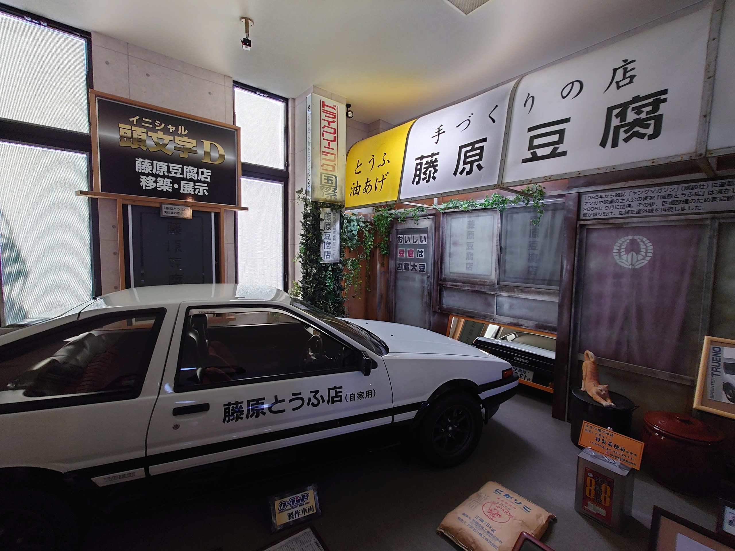 「藤原豆腐店」の看板と白黒のスポーツカーの展示