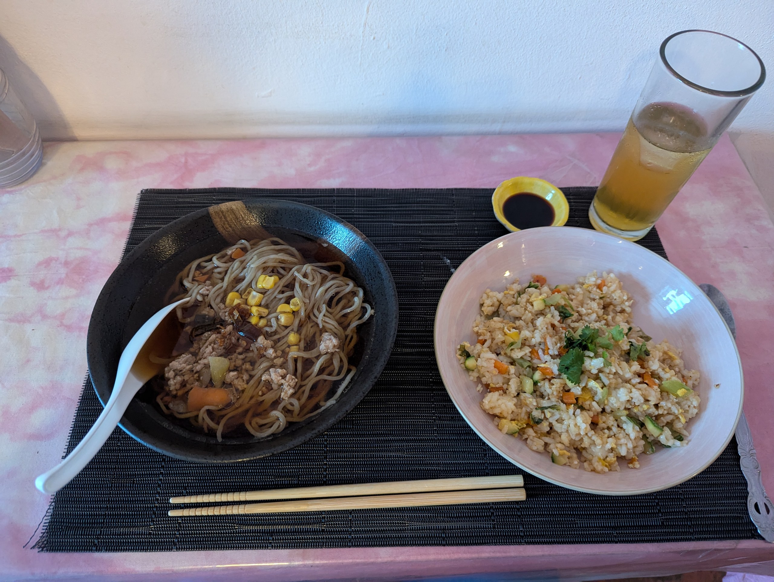 黒いトレーにのった麺の器とご飯もの、箸とビール