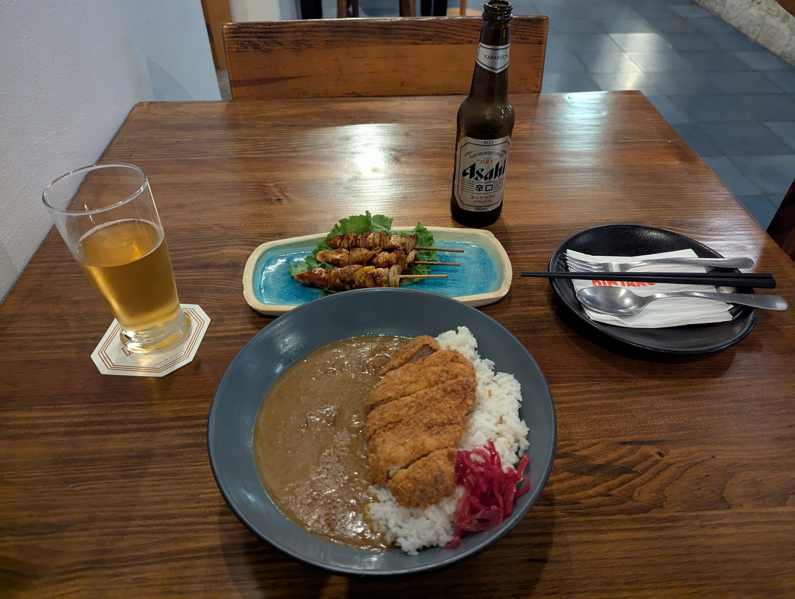 カツカレーの皿と、串焼き、アサヒビールの瓶とグラス