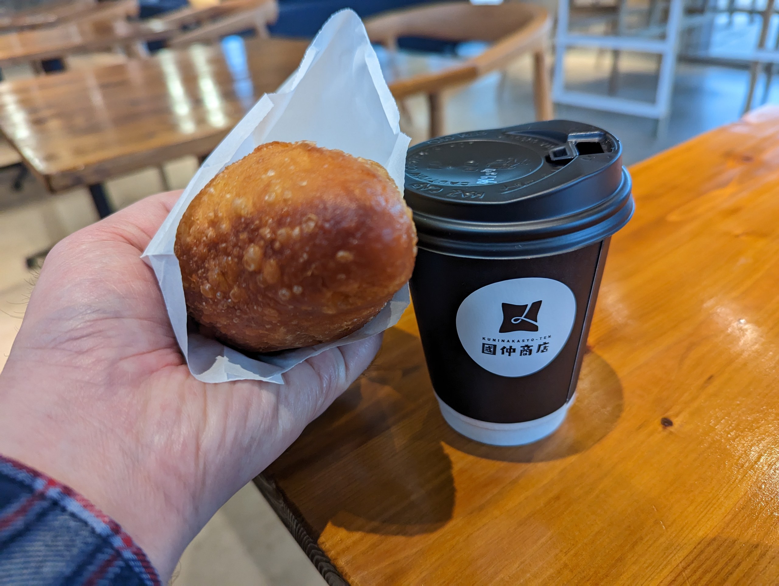 手に持った揚げパンと、國仲商店のロゴ入りのコーヒーカップ