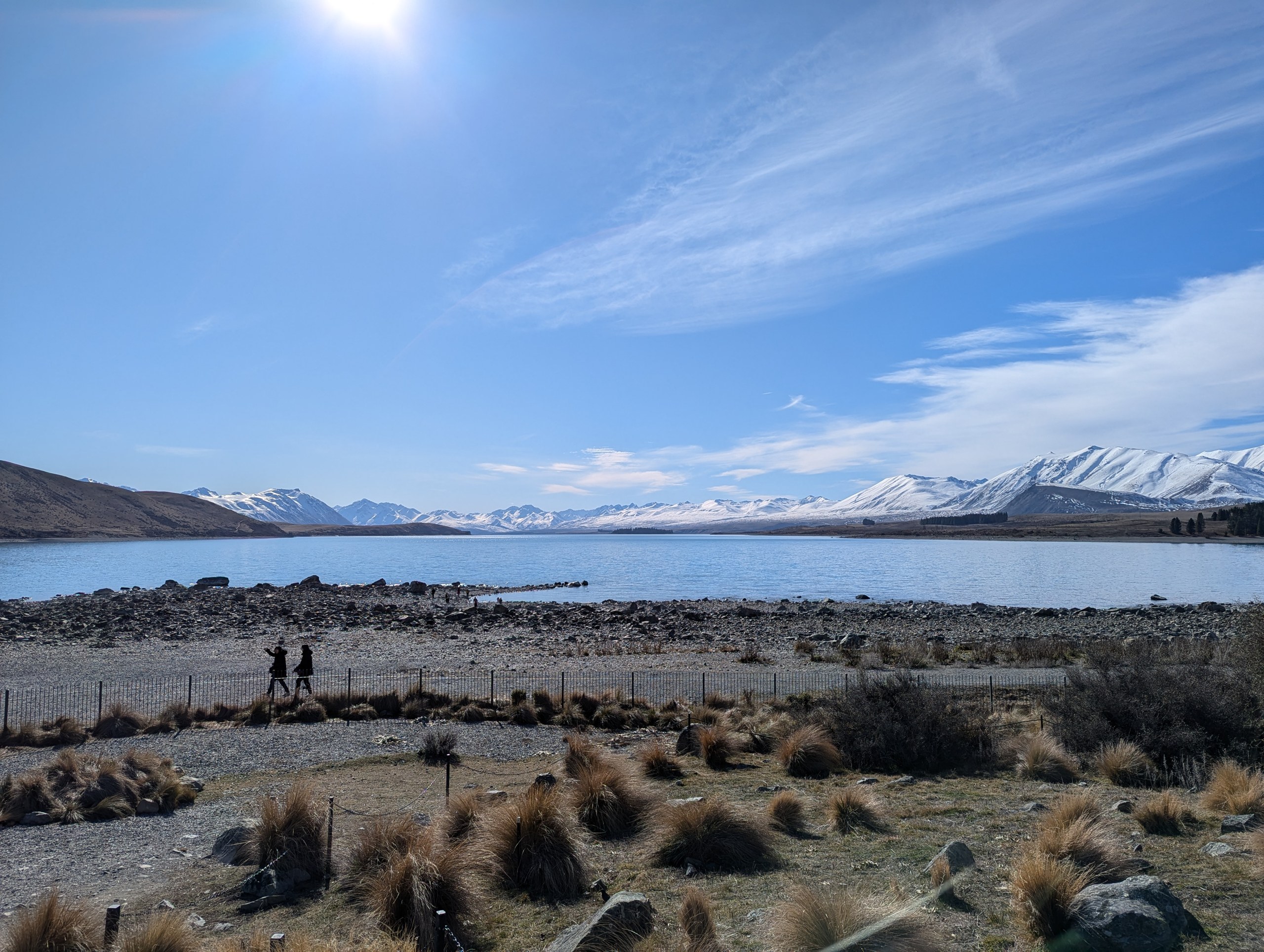 石ころの浜の向こうに広がるテカポ湖と、雪をかぶった山並み