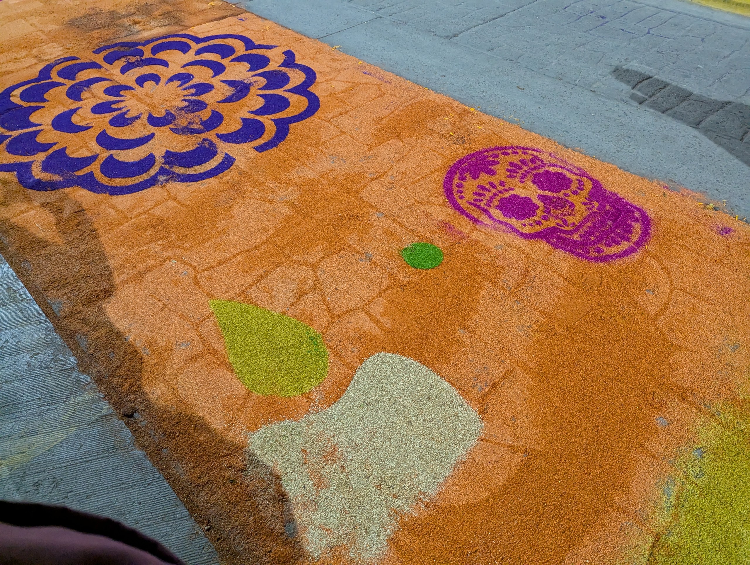 道路に色の砂で描かれた紫の花とガイコツの模様