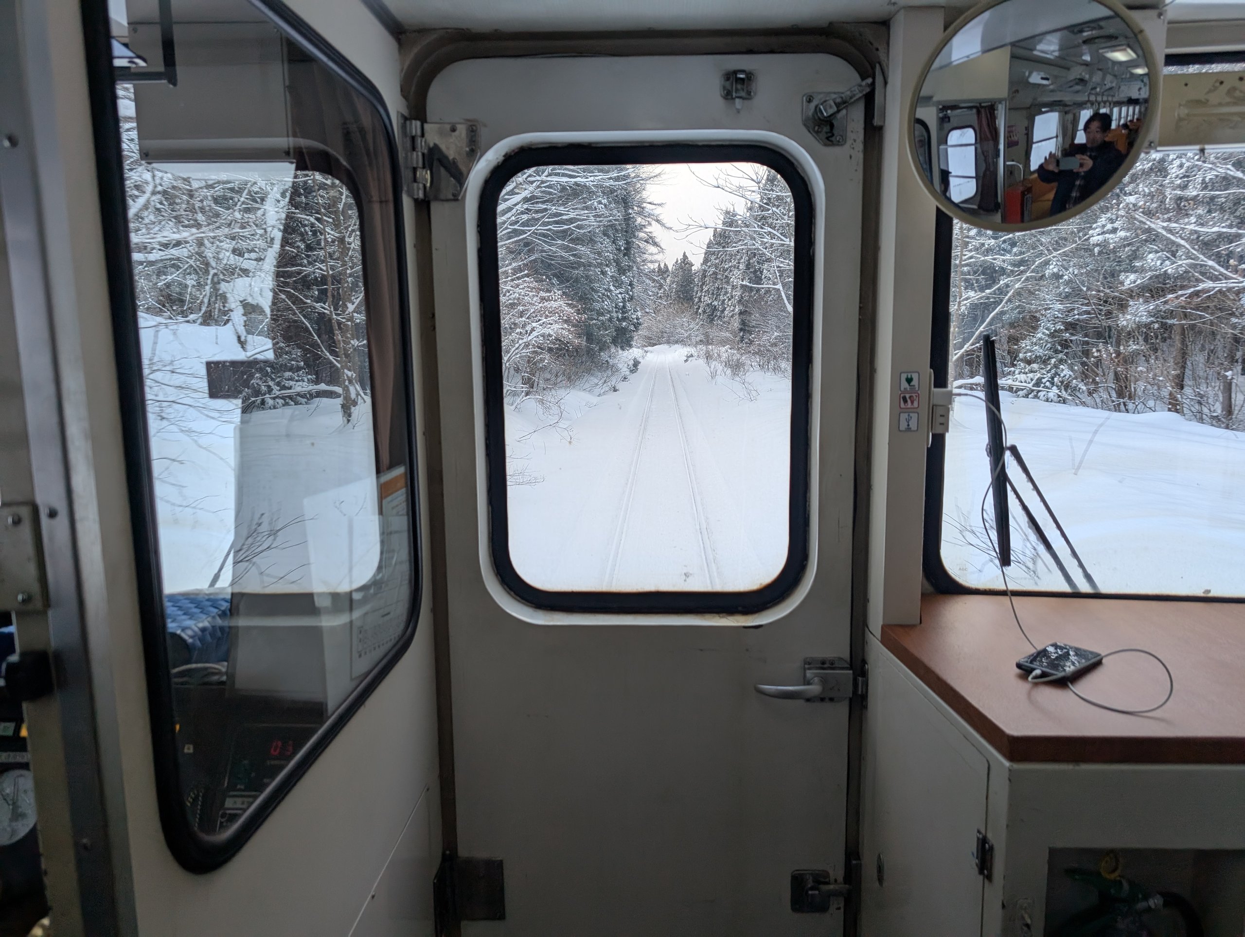 運転席の窓の向こうに続く、雪に埋もれた線路と森