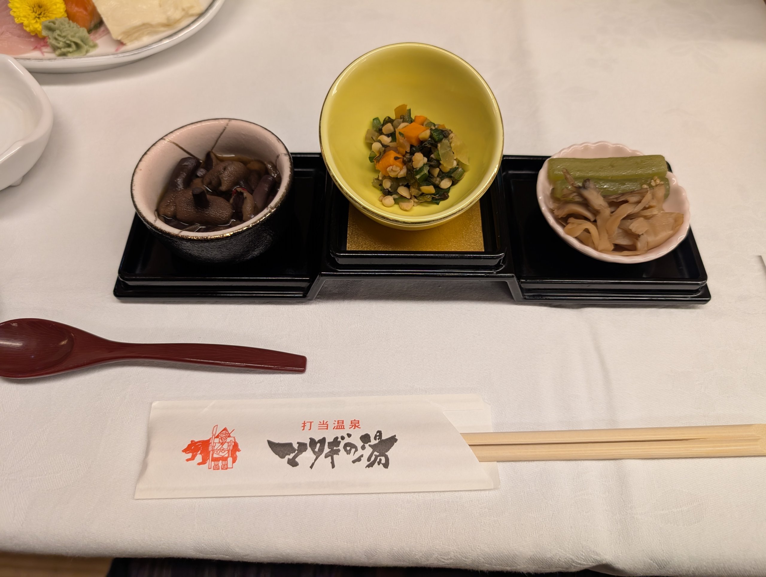 小鉢に盛られた山菜などの料理と、「打当温泉 マタギの湯」の箸袋
