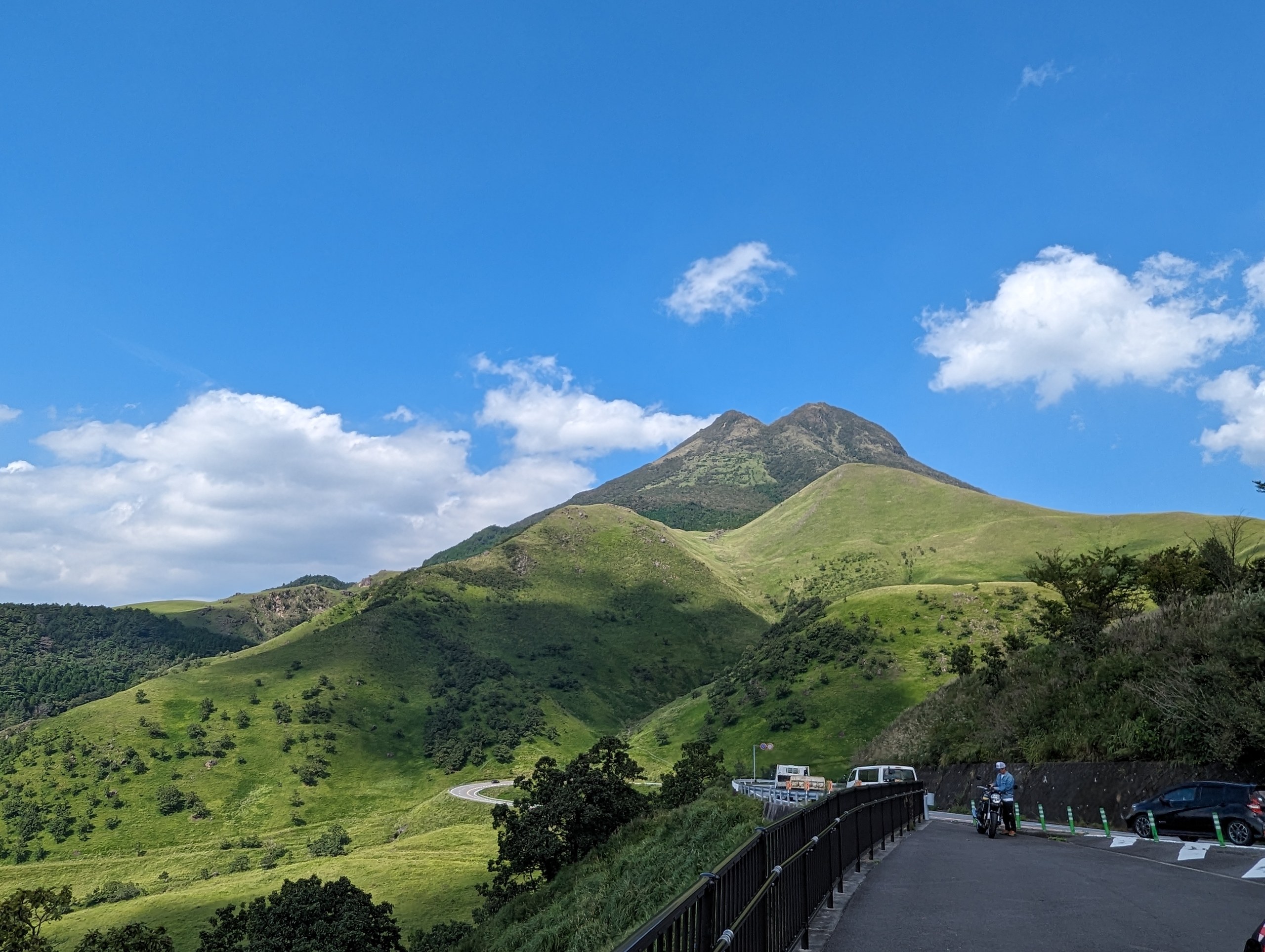 青空の下、緑の草原の上にそびえる由布岳