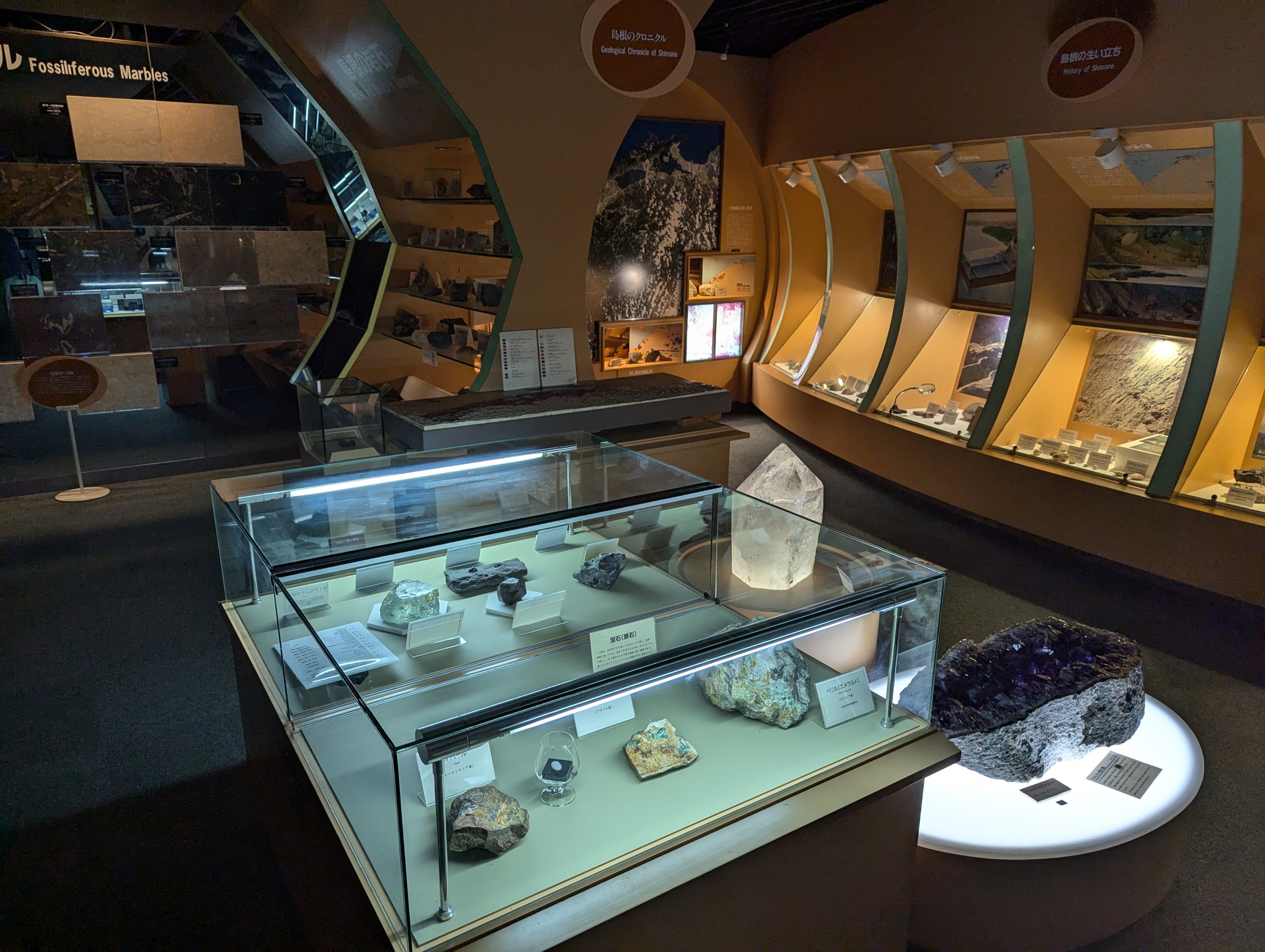 夜の展示室で、ライトに照らされた鉱物や結晶のケースと「島根のクロニクル」の展示