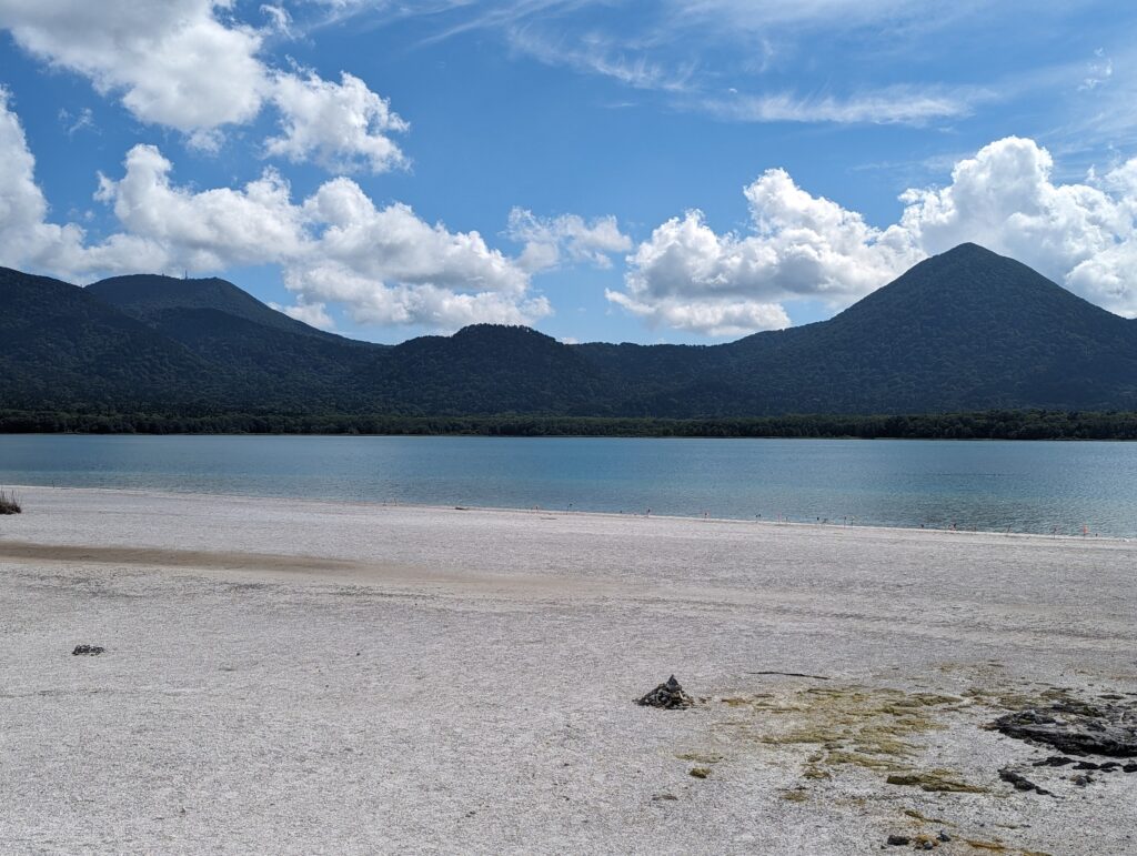 白い砂浜の先に広がる宇曽利山湖と、三角の山