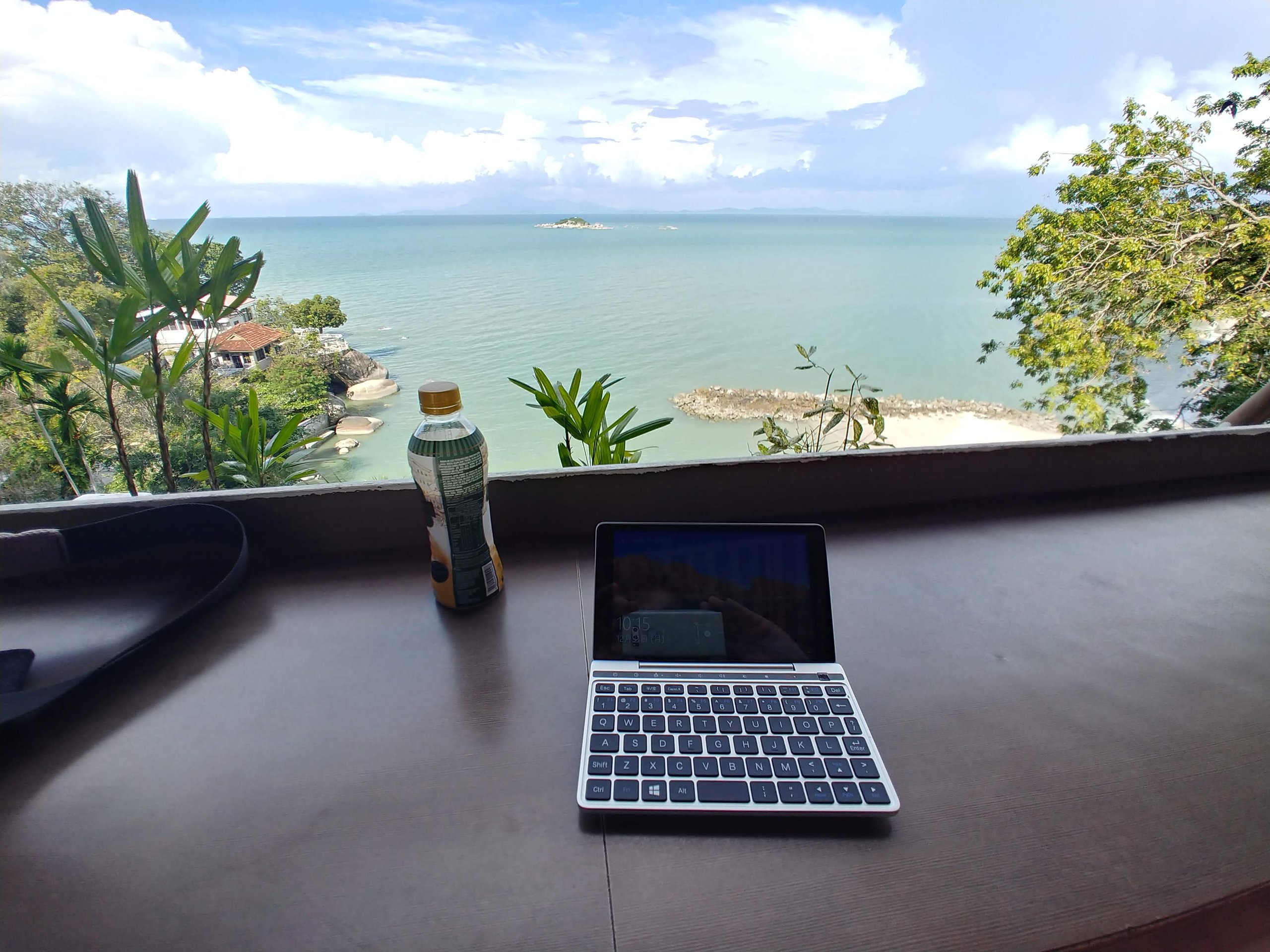 テーブルのノートパソコンと飲み物の向こうに見える海と島