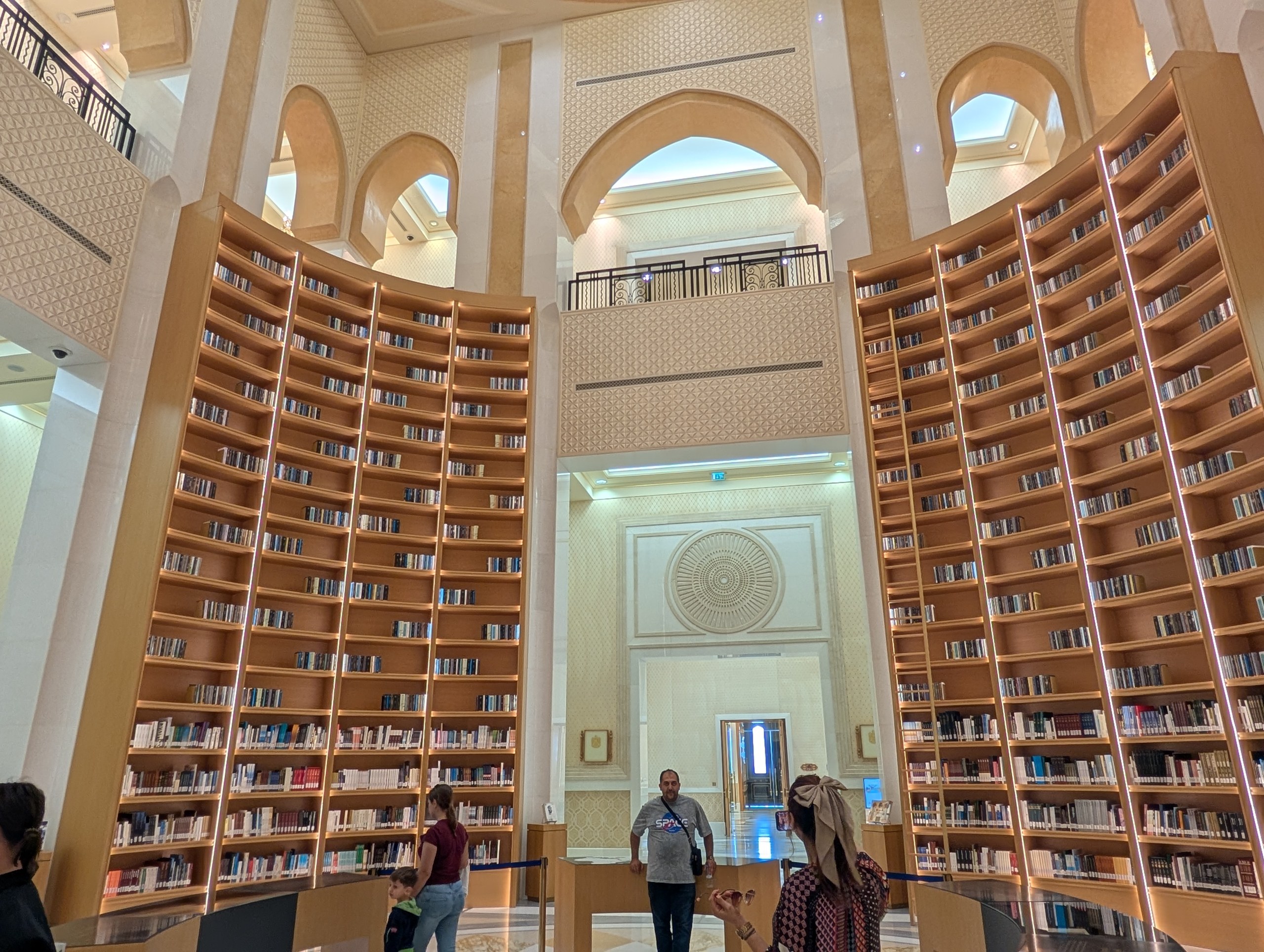 両側に弧を描く高い本棚と、奥のアーチ窓のある図書館