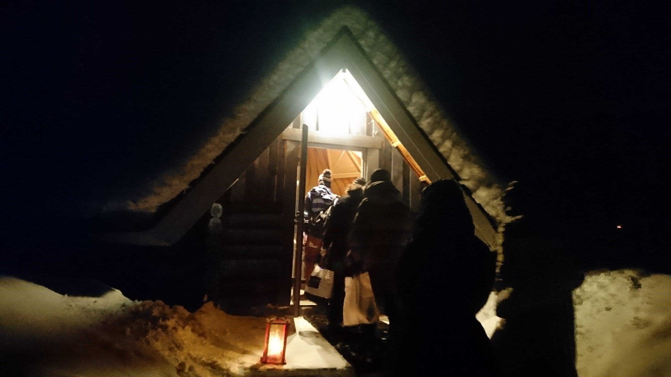 オーロラツアーの夜、明かりのともる三角屋根の小屋