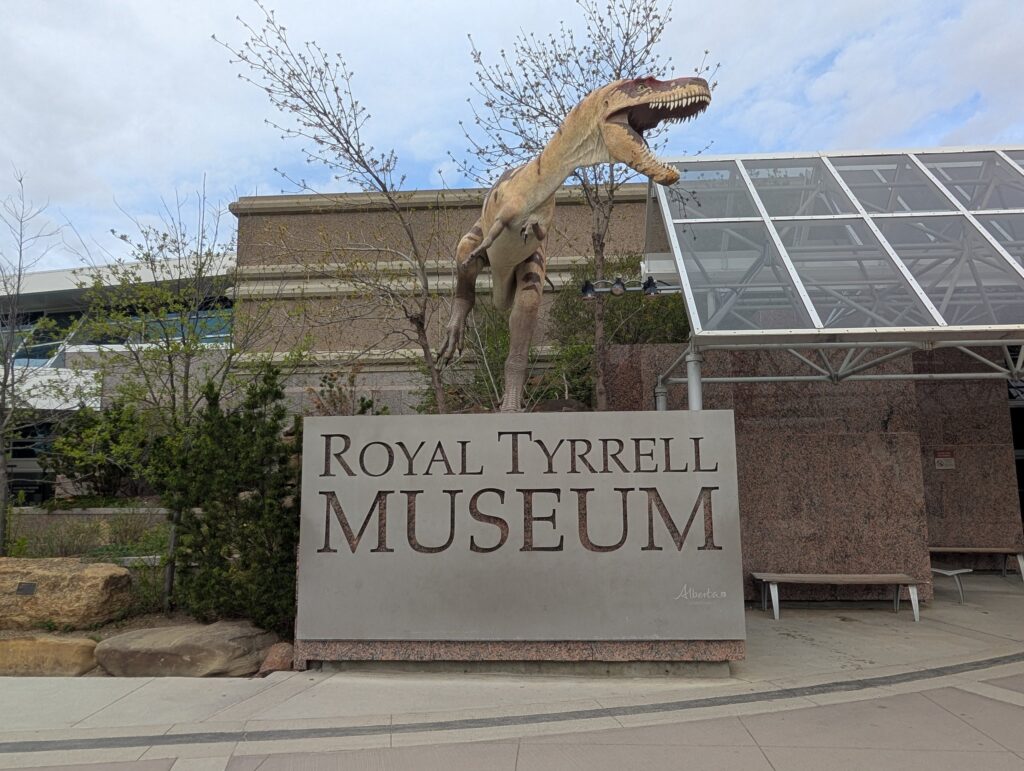 「ROYAL TYRRELL MUSEUM」の看板と、建物の前で口を開けたティラノサウルスの像