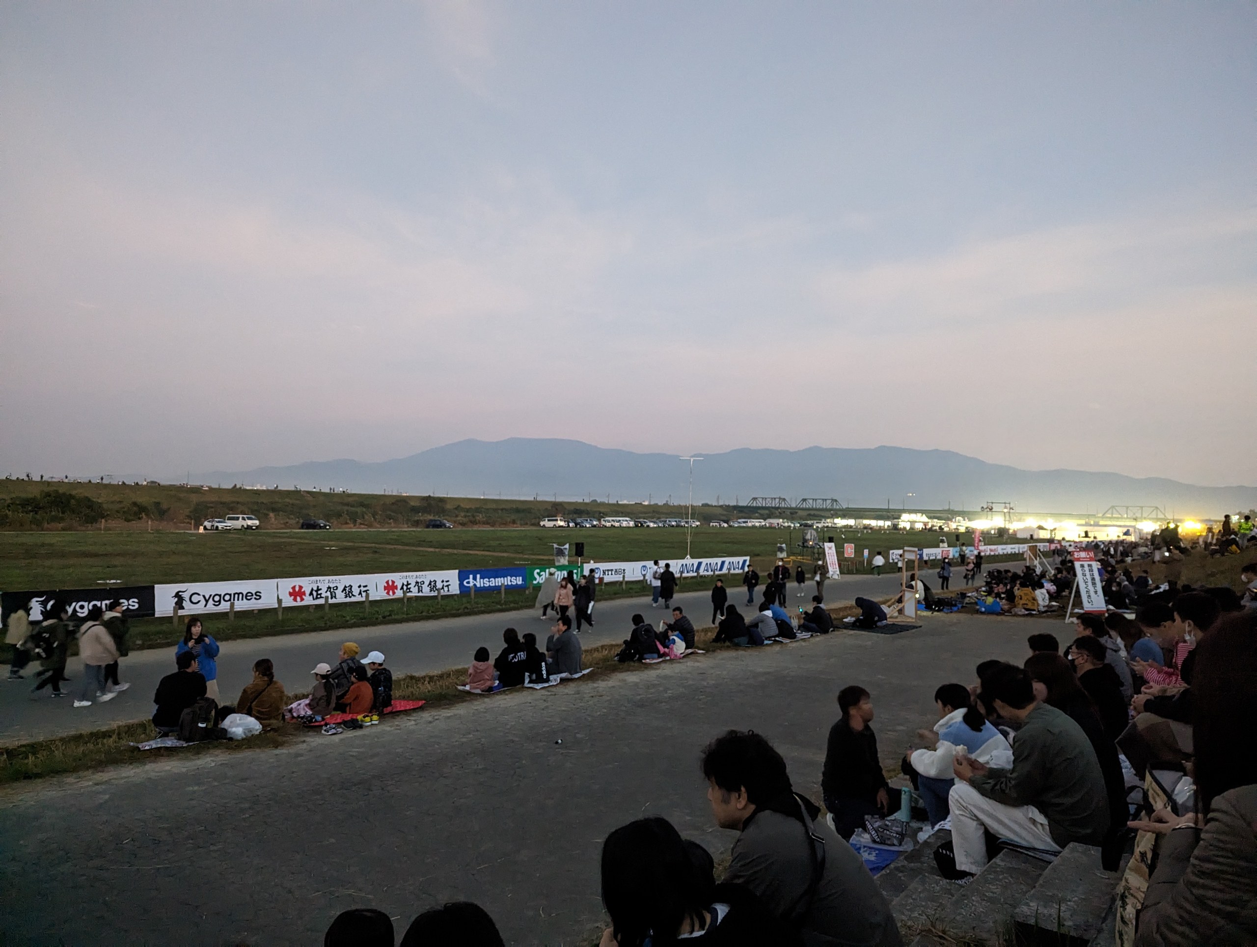 夜明けの空の下、河川敷に集まり始めた人たち