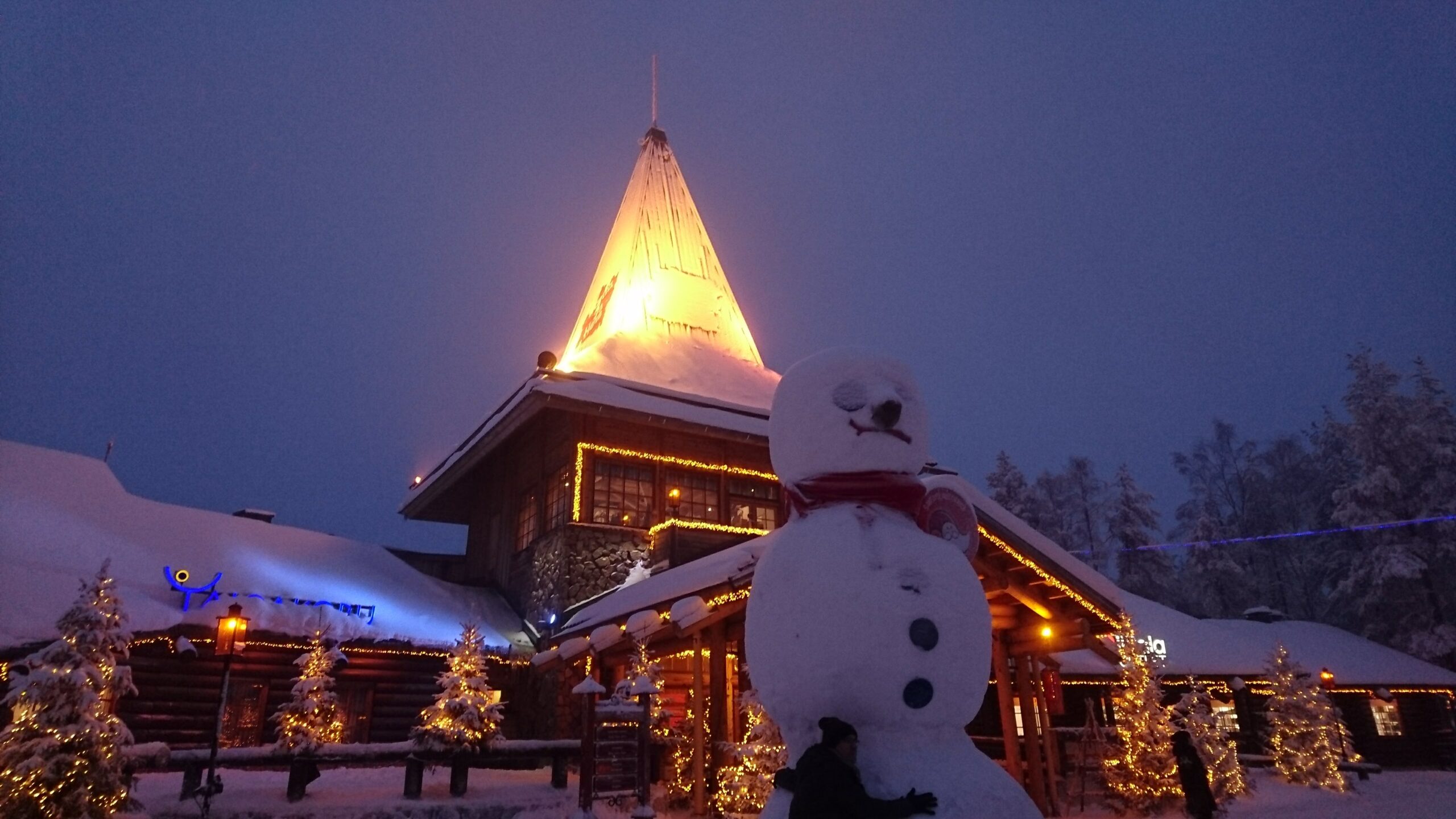 ライトアップされたサンタクロース村の三角屋根の建物と雪だるま