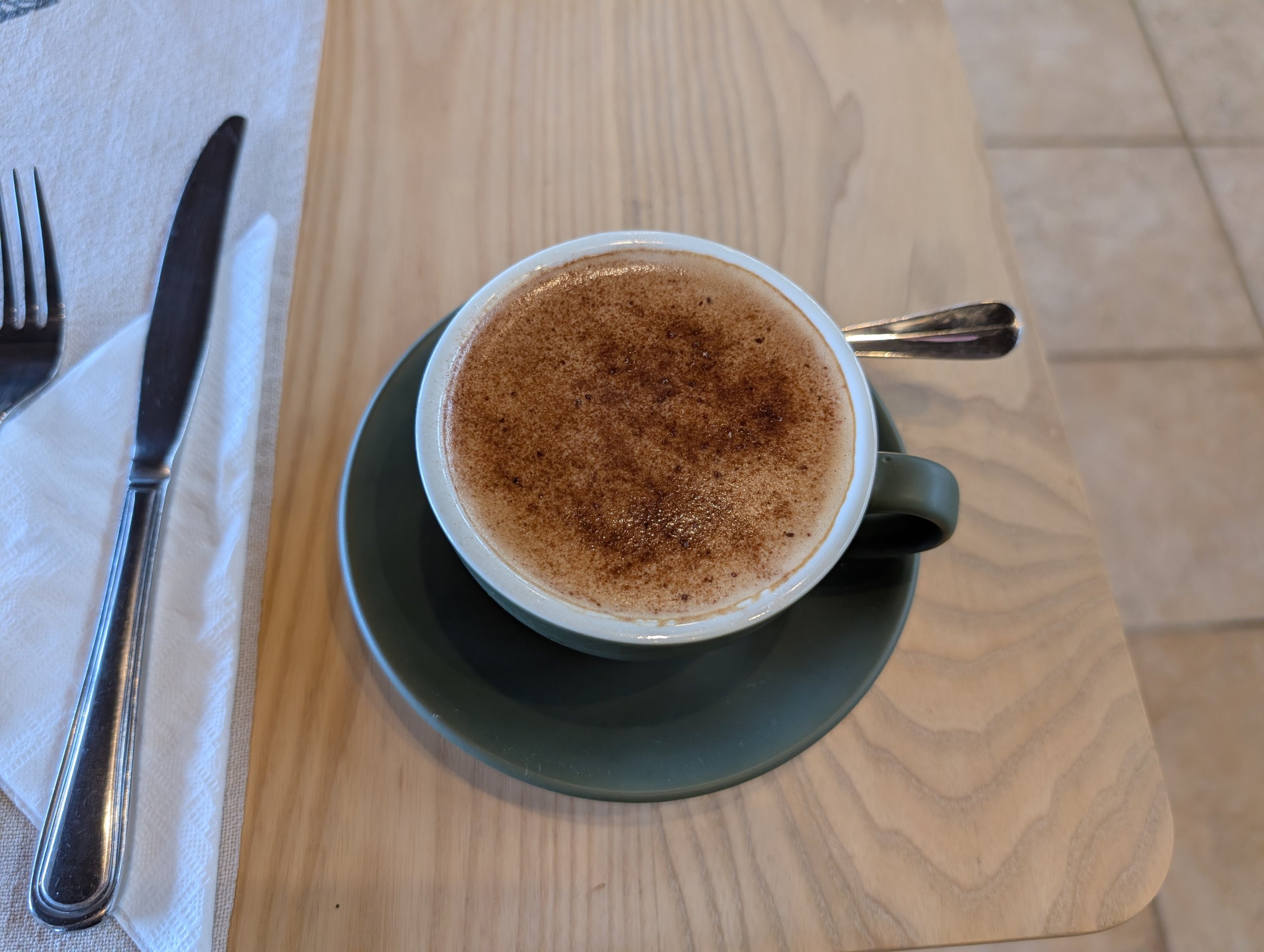 木のテーブルに置かれた、泡ののったコーヒー