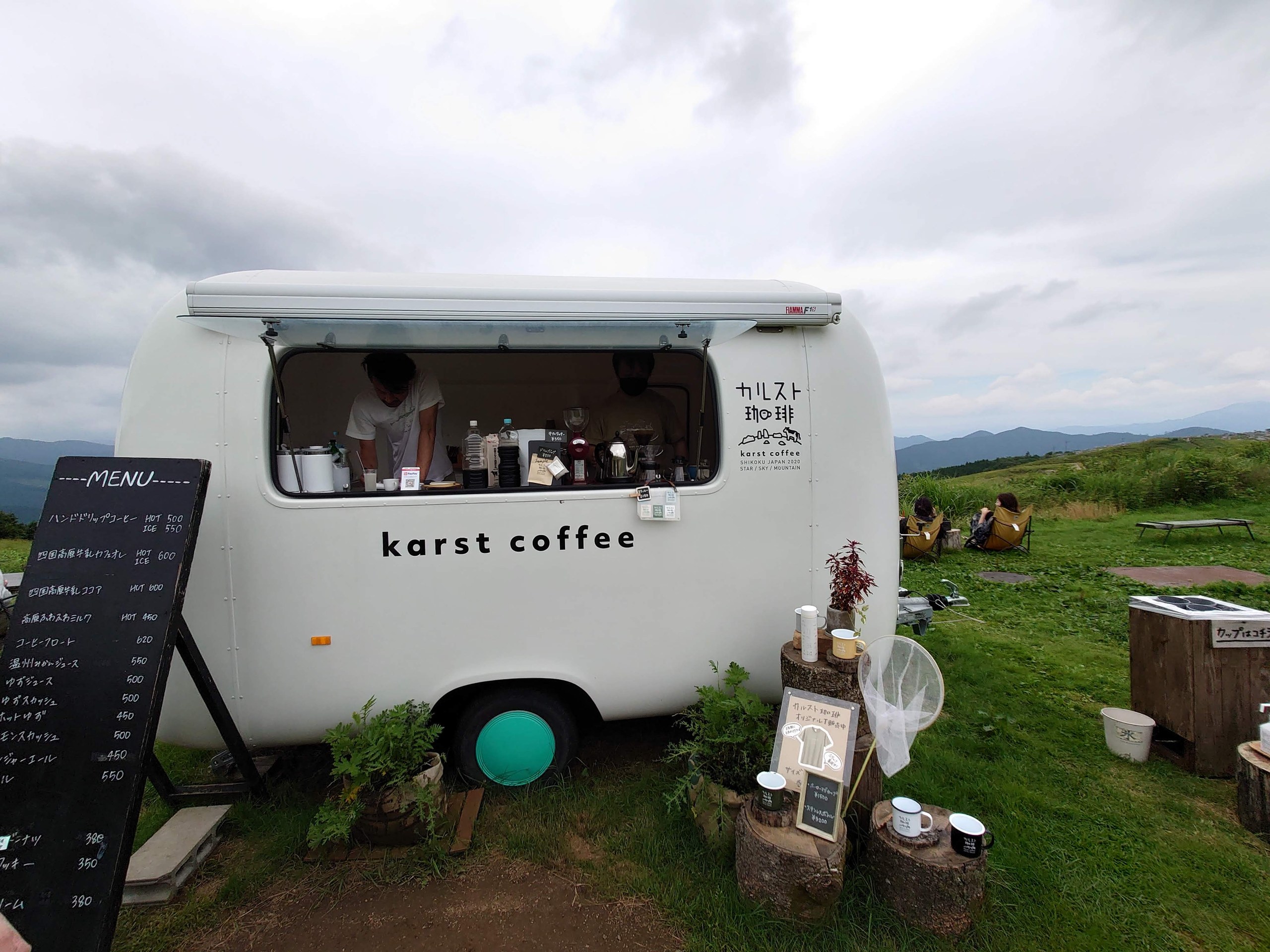 草原に停まる白いキッチンカー「karst coffee」とメニューの黒板