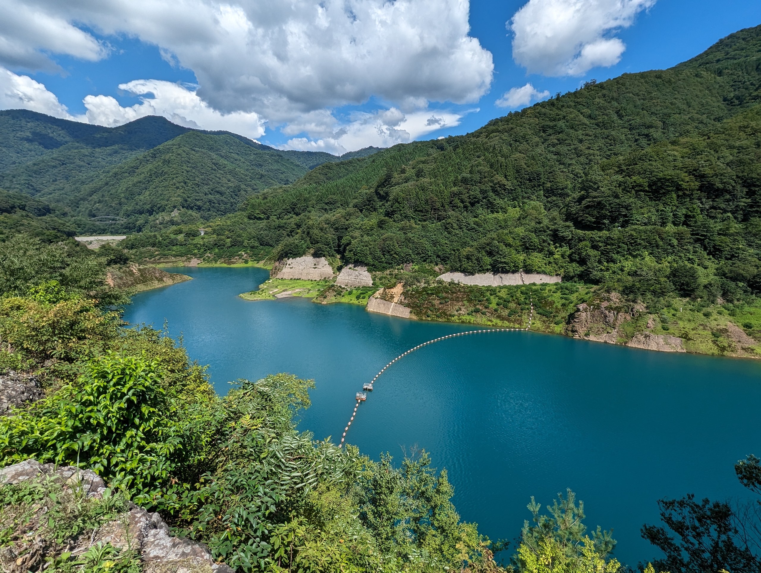 夏の青空の下、緑の山に囲まれた青い奥四万湖