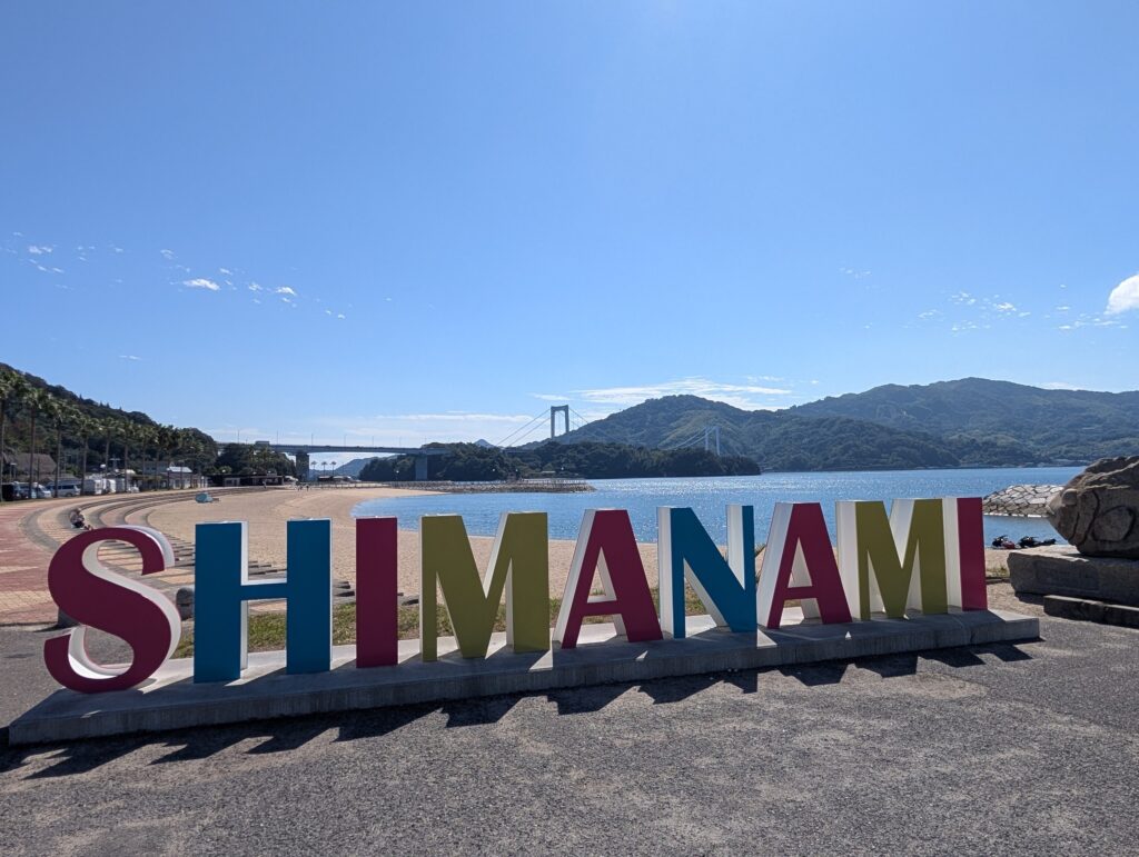 カラフルな「SHIMANAMI」の文字と、浜辺の向こうの橋
