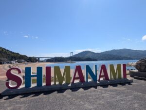 カラフルな「SHIMANAMI」の文字と、浜辺の向こうの橋