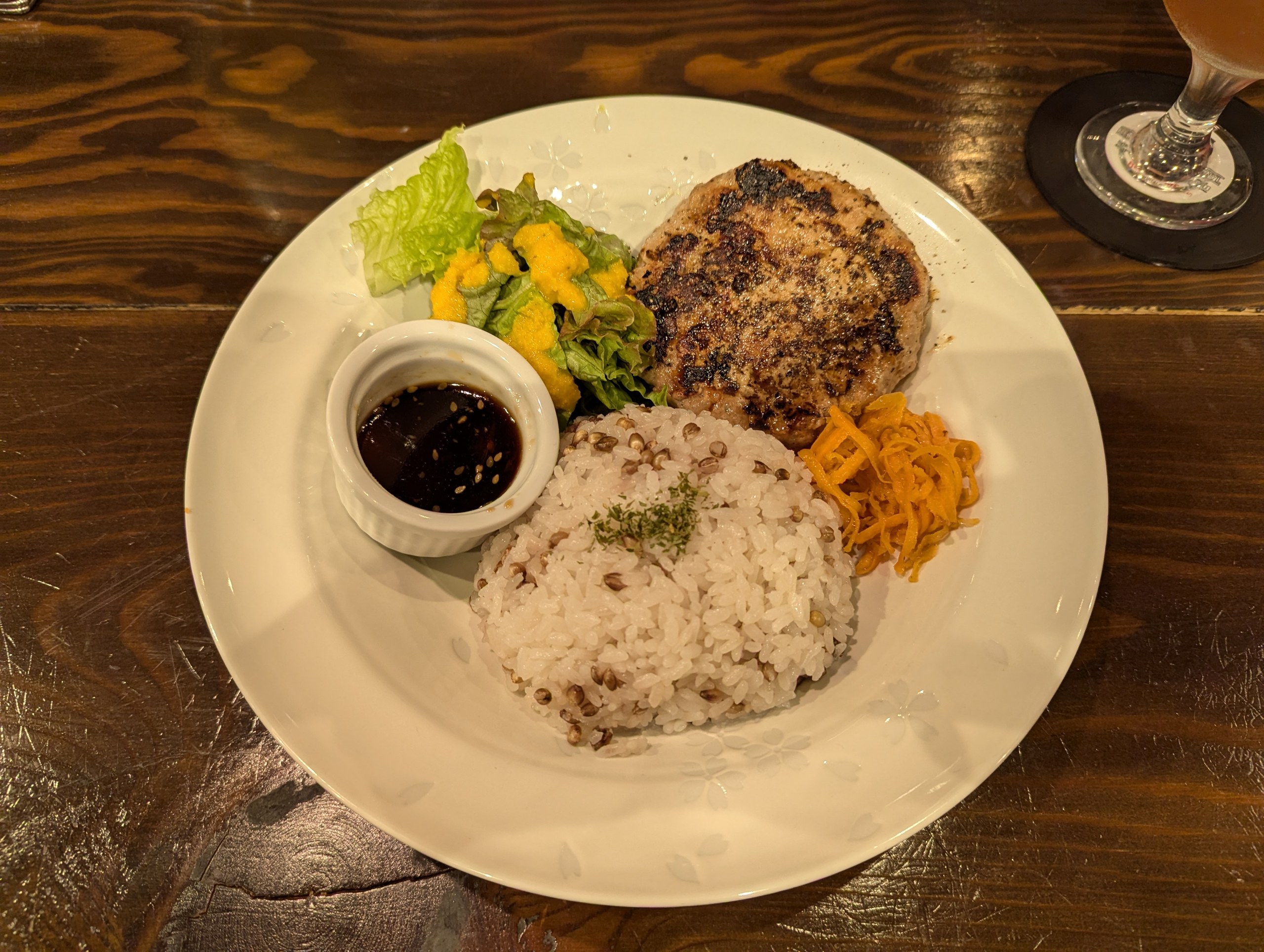 木のテーブルに置かれたハンバーグとごはん、サラダがのったプレート