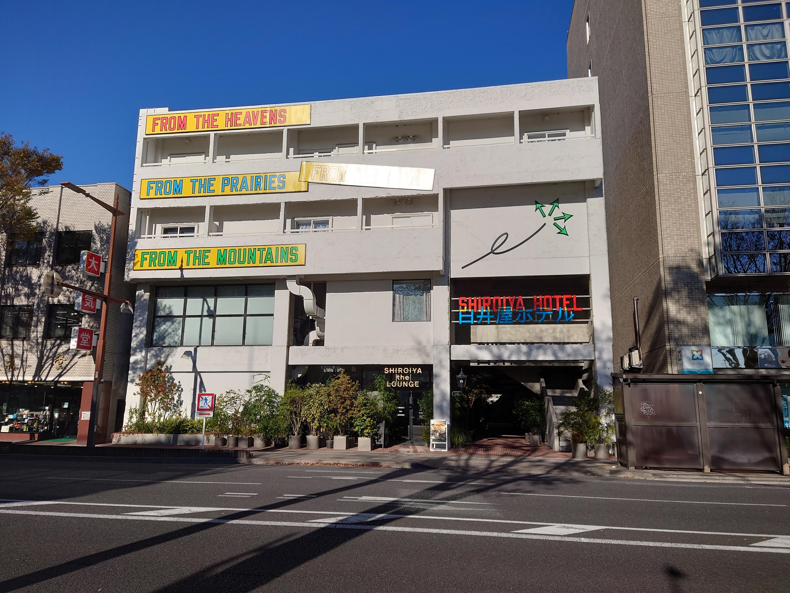 通りに面したSHIROIYA HOTELの白い建物と英語のネオンサイン
