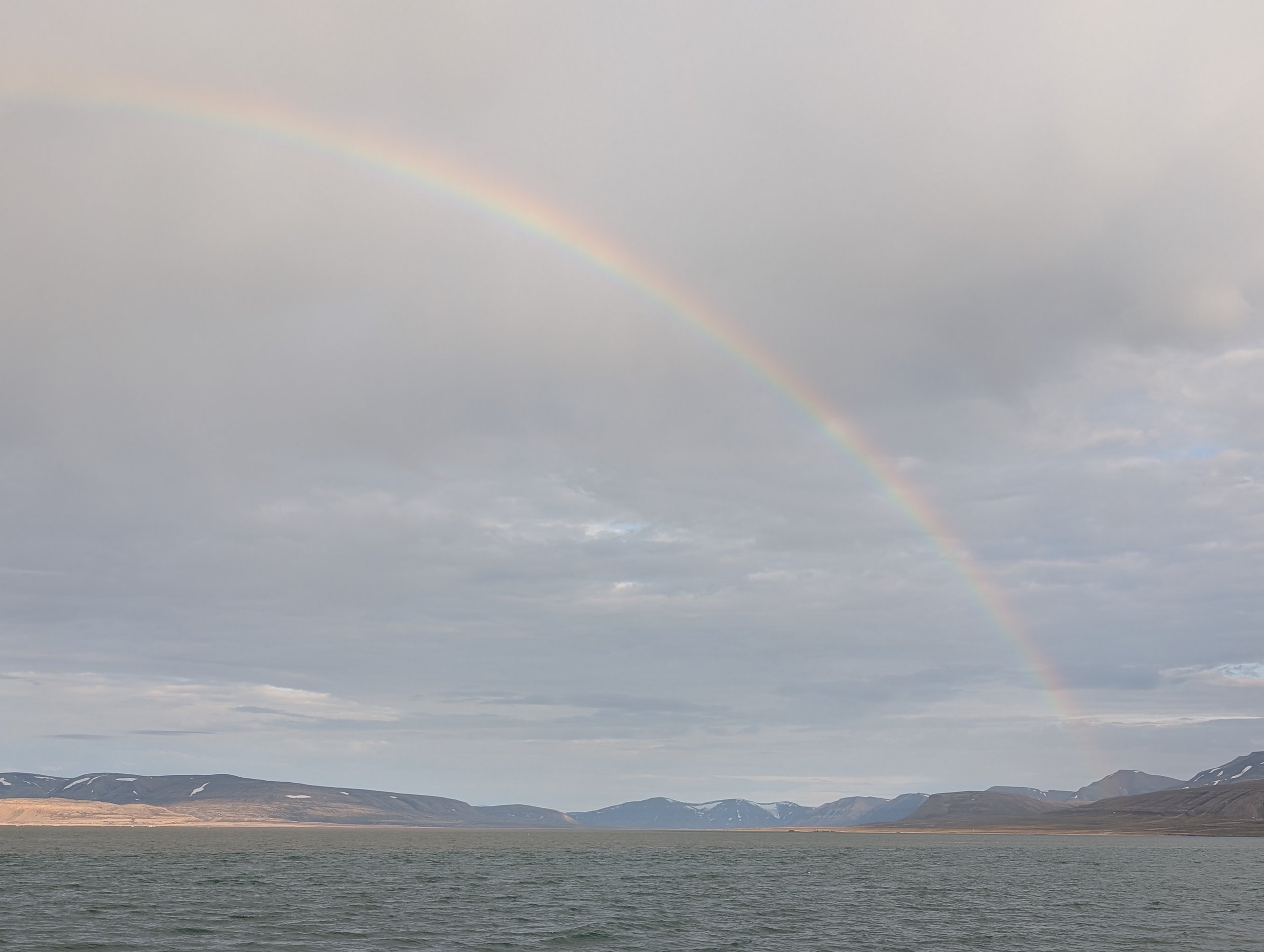 曇り空の海の上にかかる虹と、その付け根