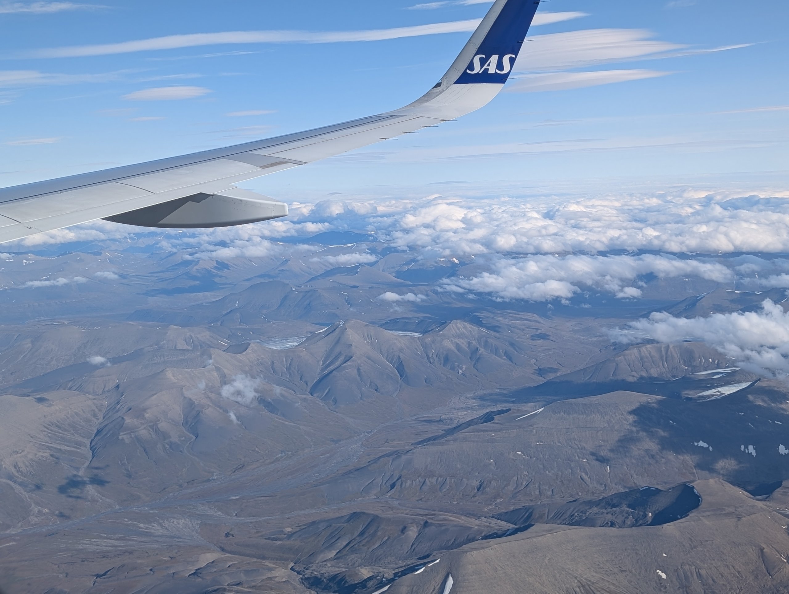 飛行機の翼の下に広がる、雪の残る山と雲