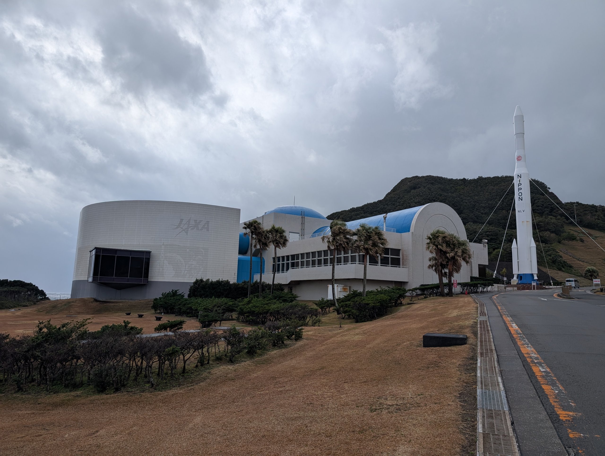 白い建物と青いドーム屋根の宇宙科学技術館と、その横に立つロケット