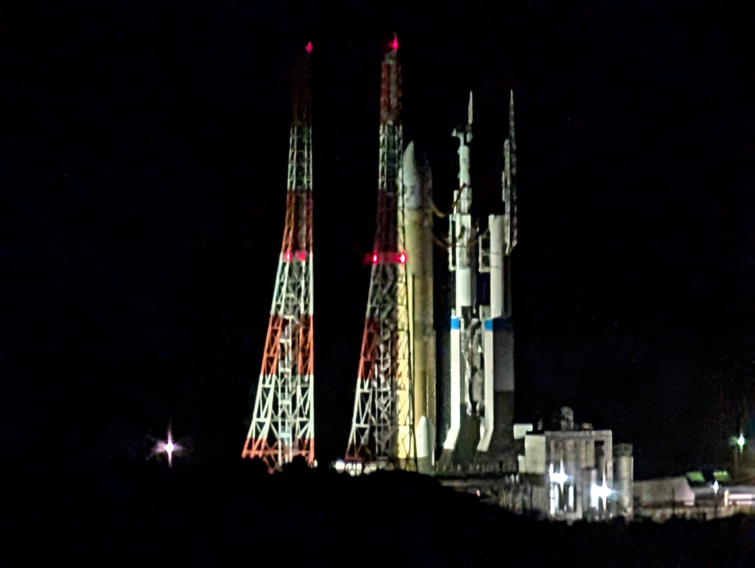夜の発射台にライトアップされて立つH3ロケットと、赤白の塔