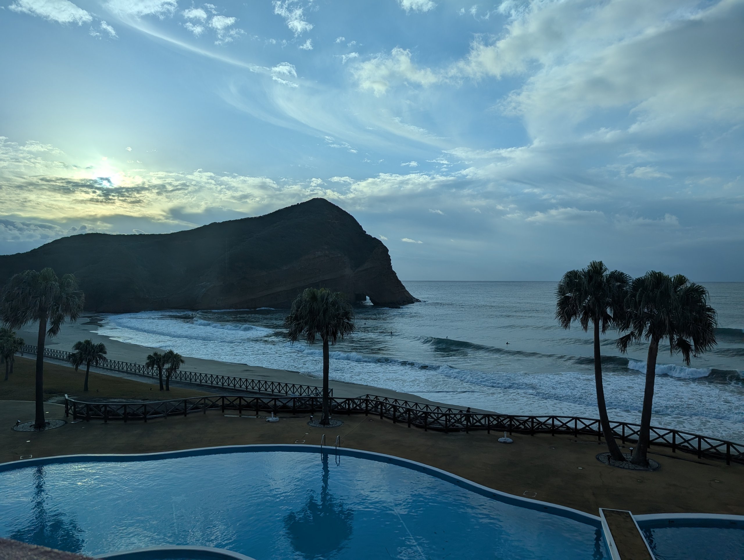 朝のプールとヤシの木、その向こうの海と岩山