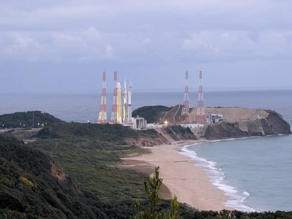 入り江と砂浜の向こうの岬に立つ、発射台とロケット